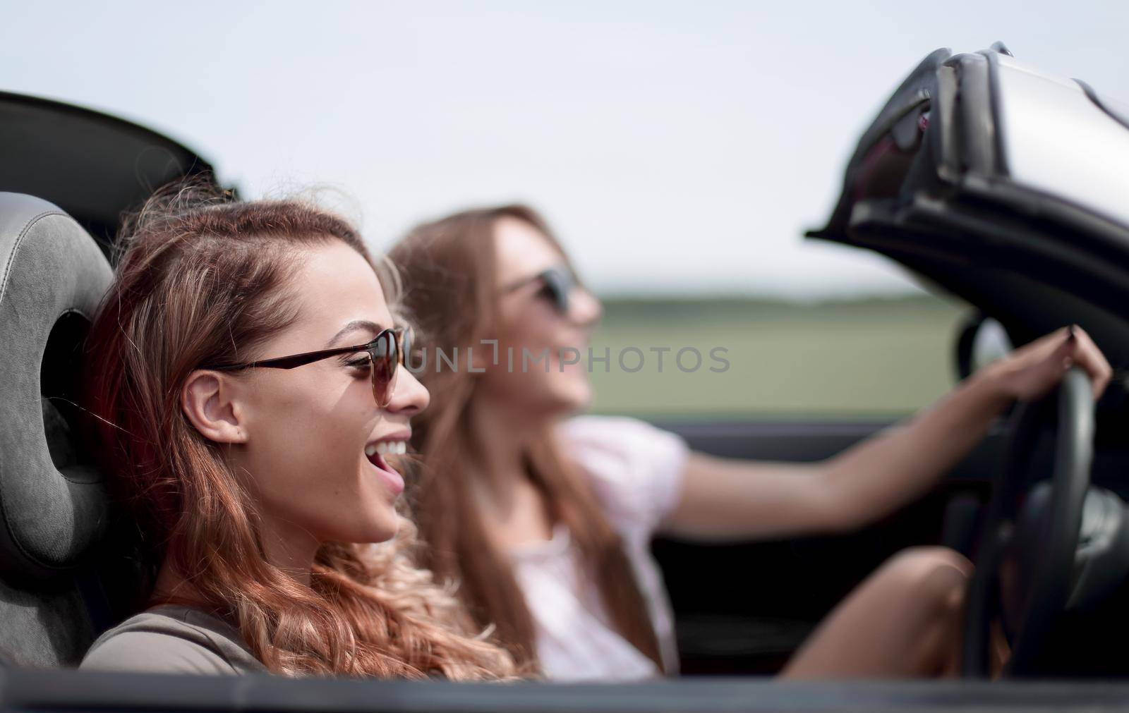 two fashionable girls travel in a convertible car. by asdf