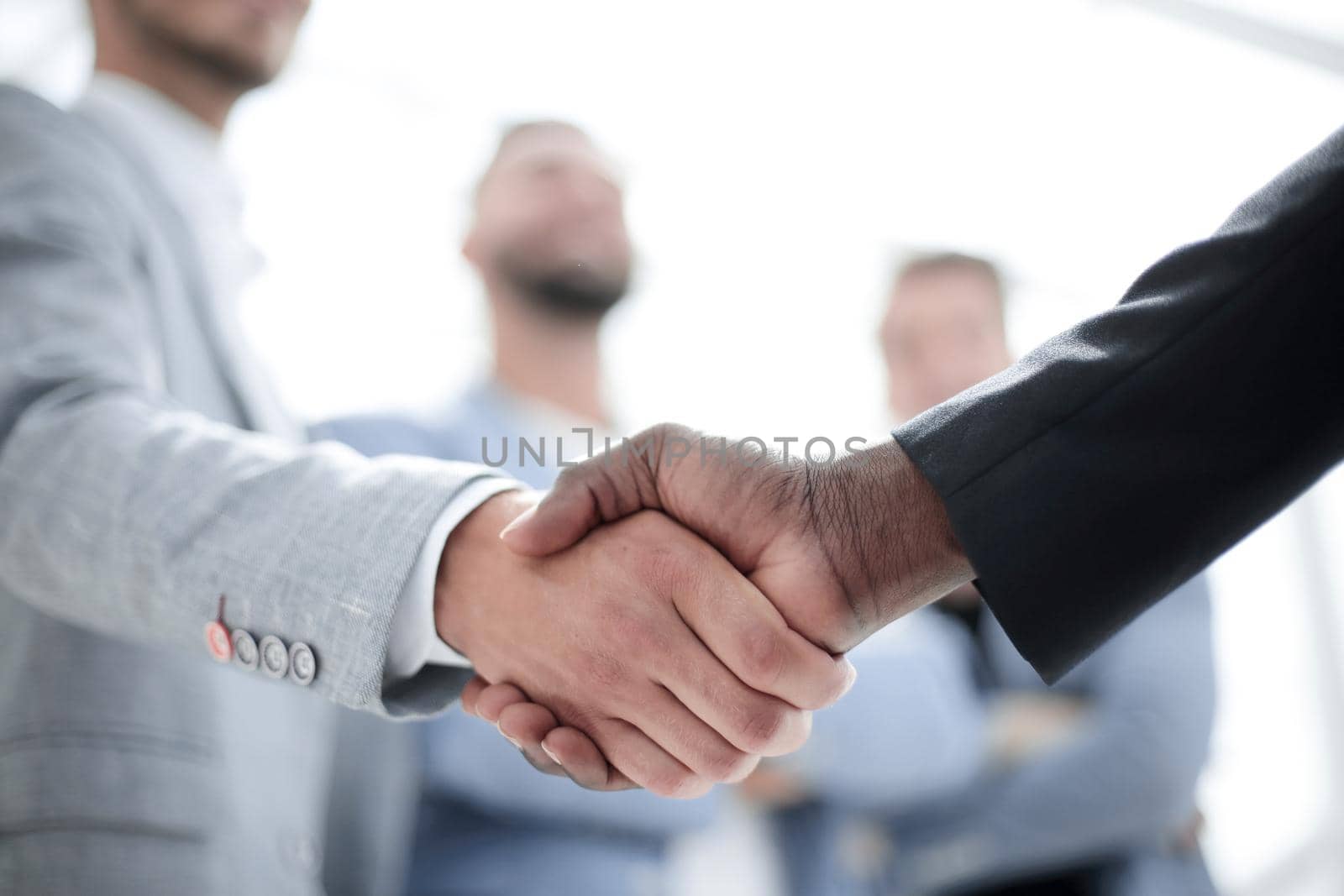 Two businessmen in suits shaking hands at group meeting, partners handshaking at negotiations making deal or signing contract