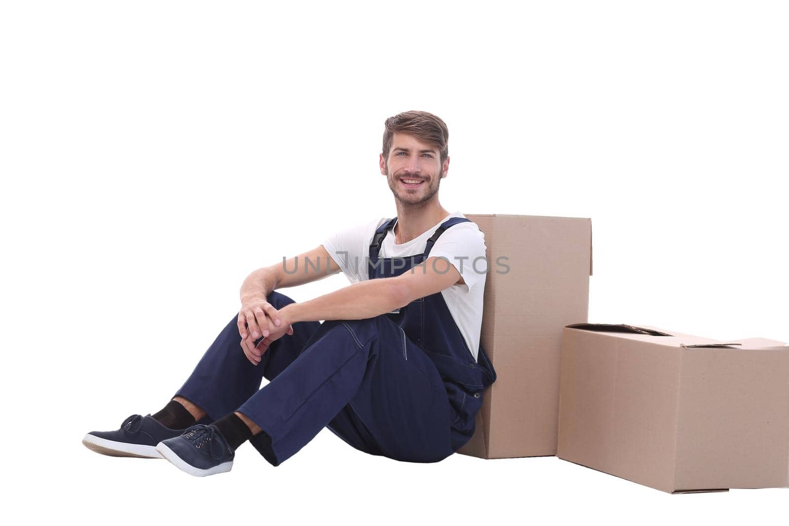 in full growth. smiling man sitting near cardboard boxes.isolated on white background
