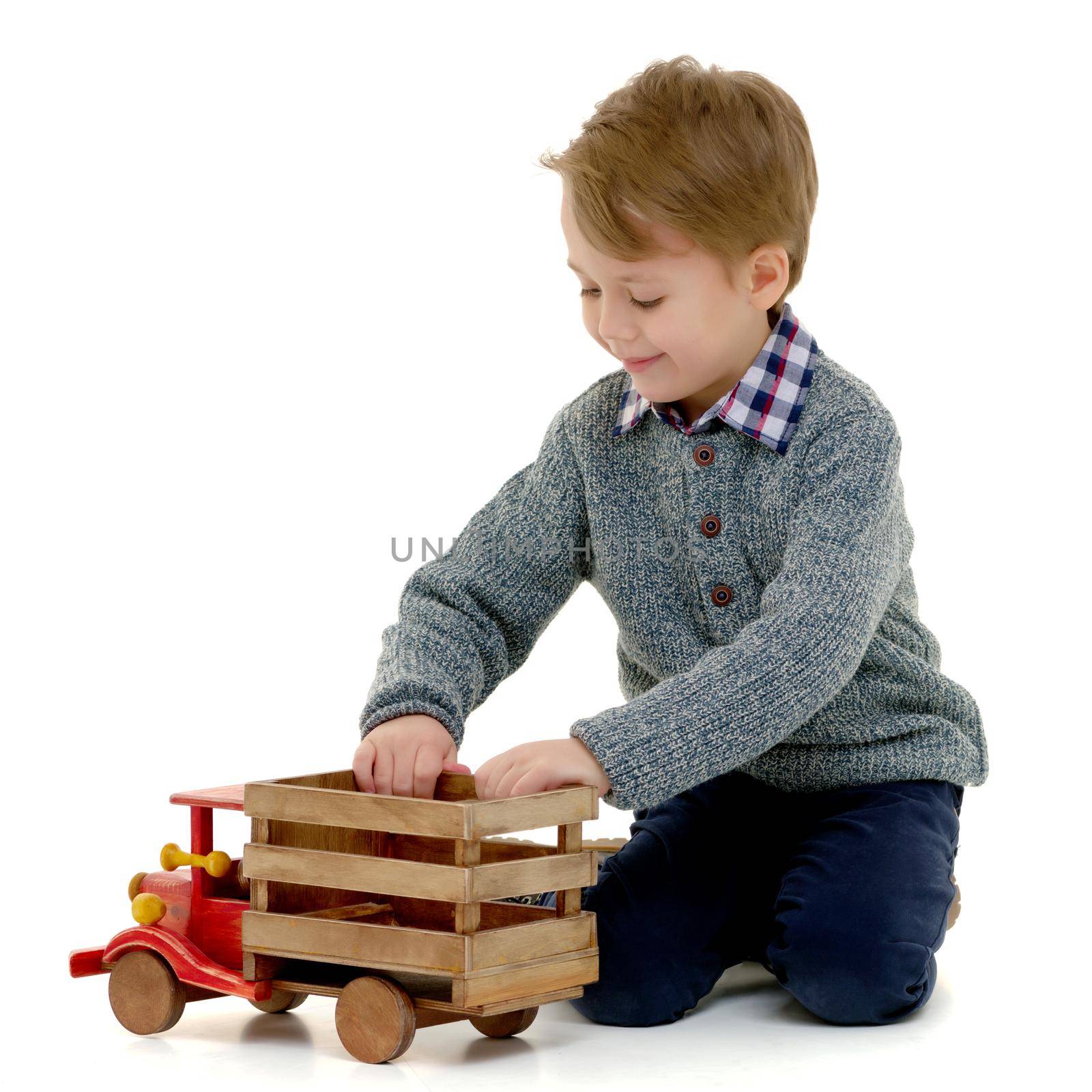 A cute little boy is playing with a big wooden car. The concept of development of a child in a family or a children's center. Advertising of children's goods and services. Isolated on white background.