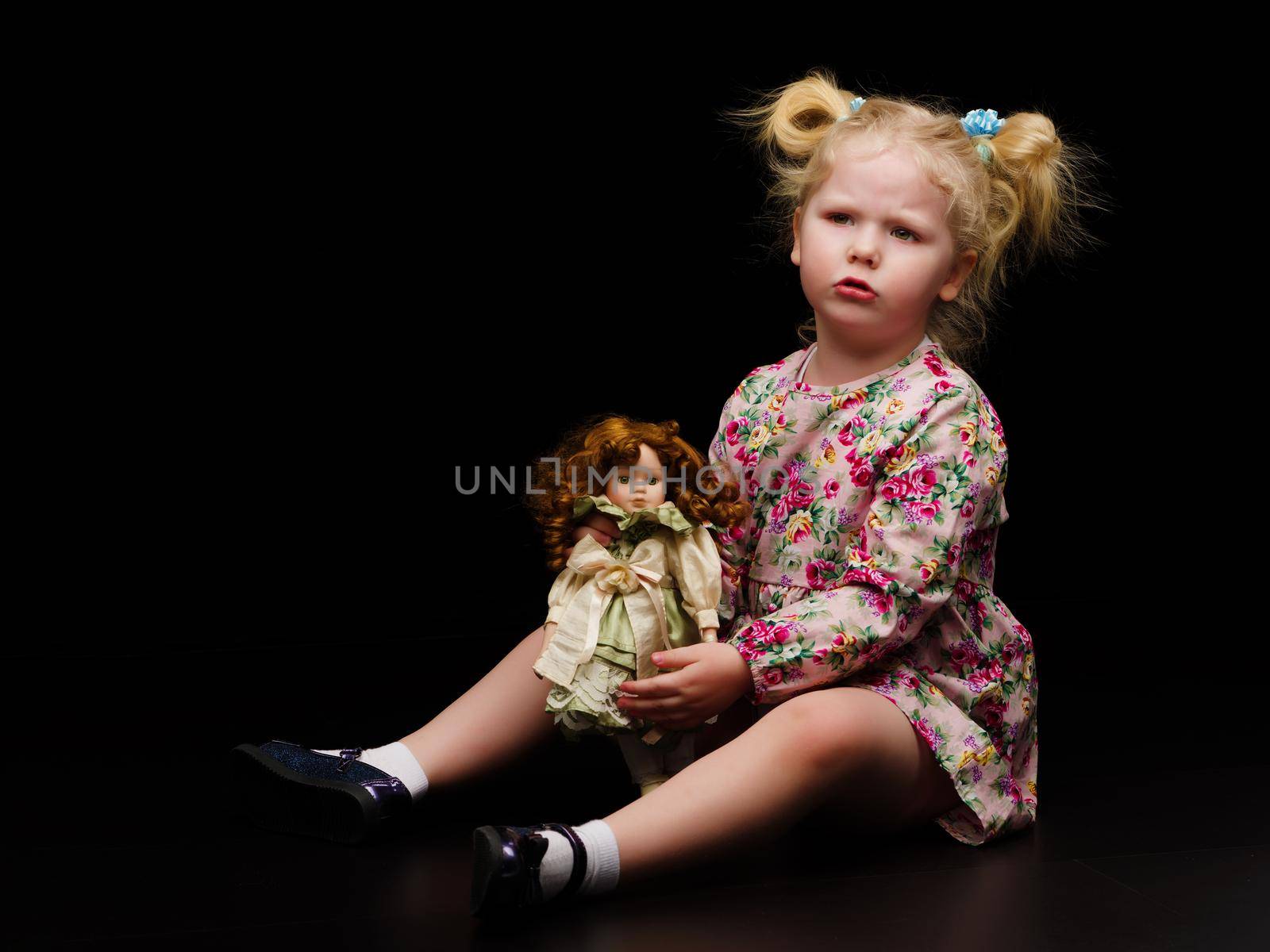 A little girl plays with a doll on a black background. by kolesnikov_studio
