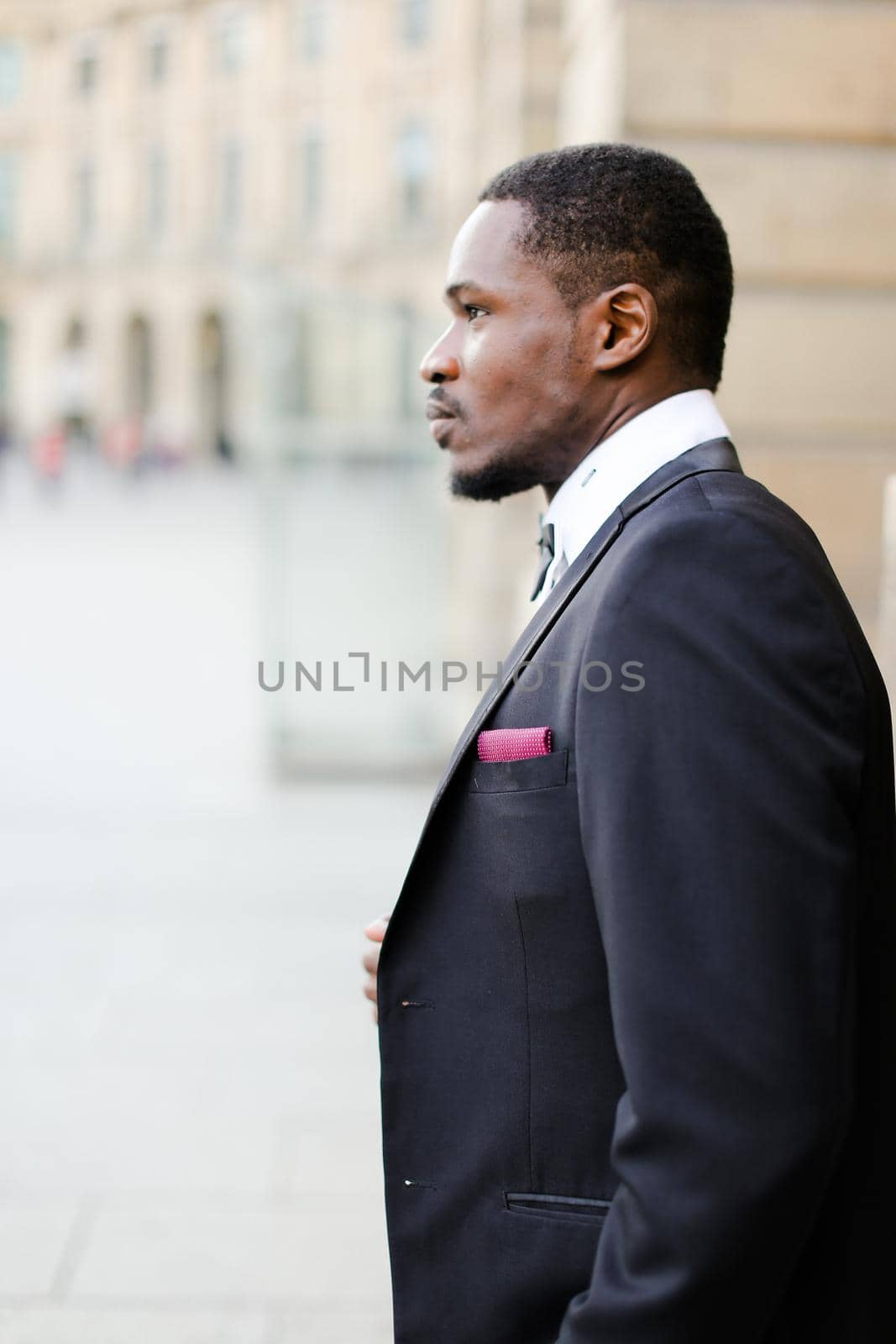 Portrait of afro american happy man wearing dark suit and standing near building. by sisterspro