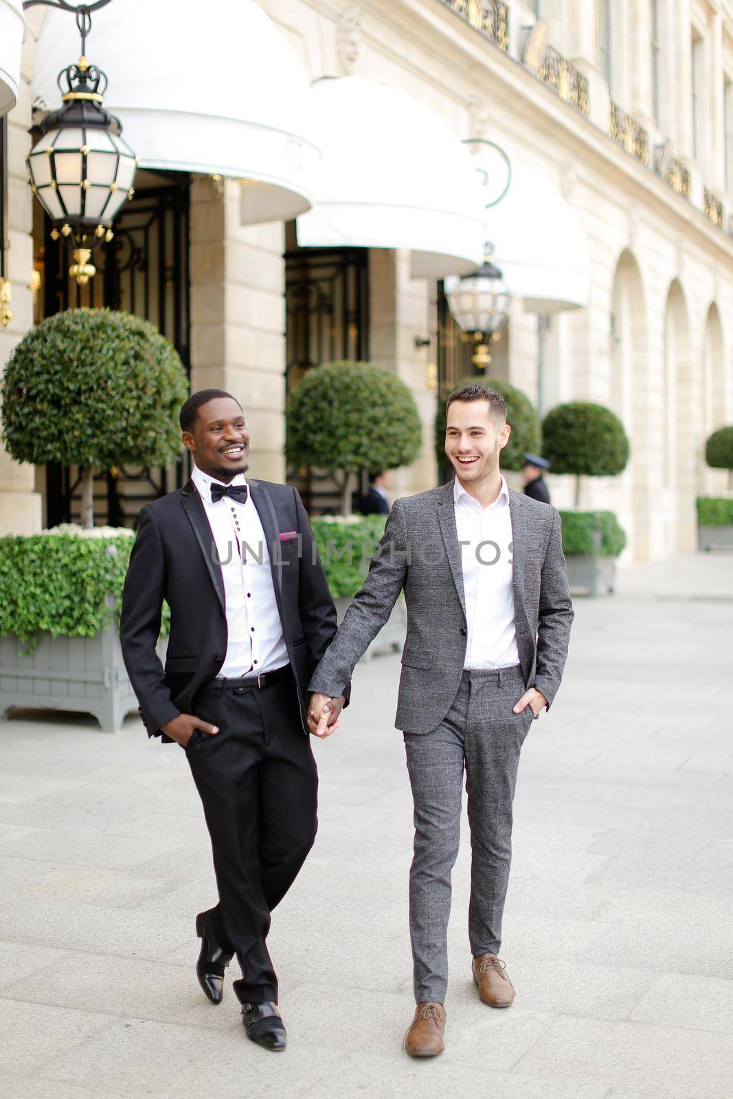 Afro american and caucasian stylish gays walking outside in city. Concept of same sex male couple.