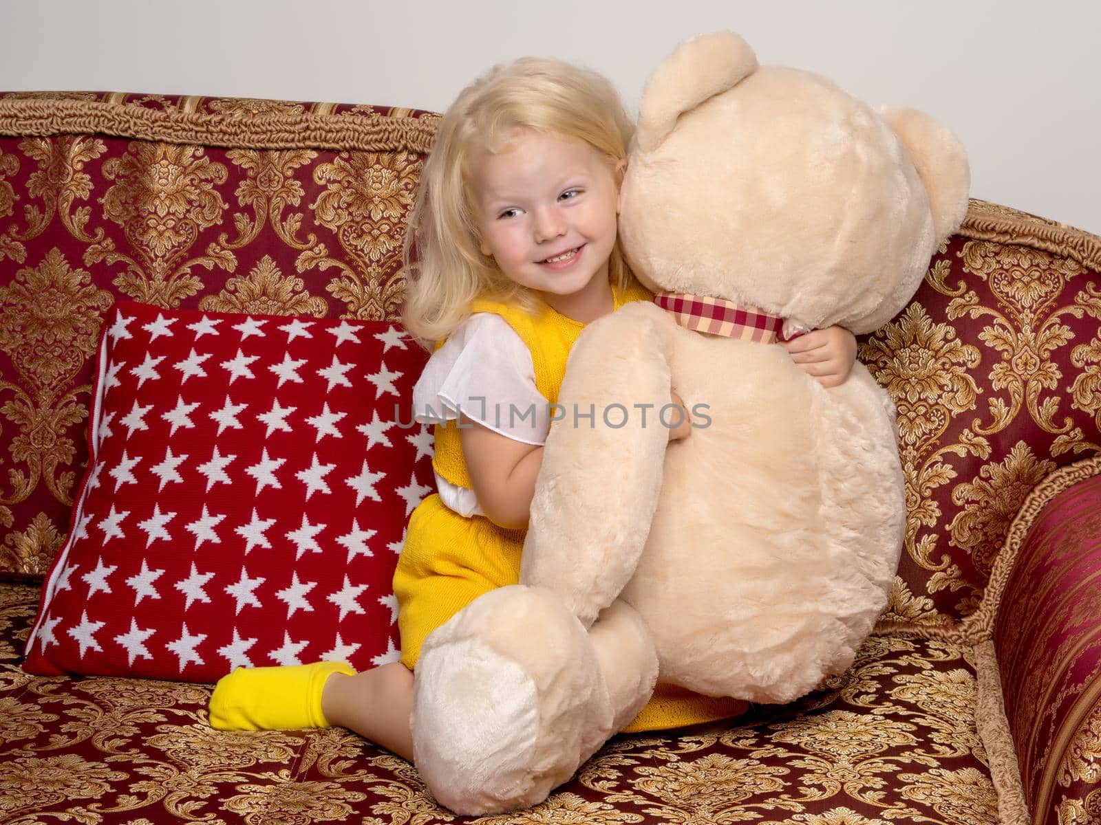 Little girl on sofa hugging teddy bear. by kolesnikov_studio