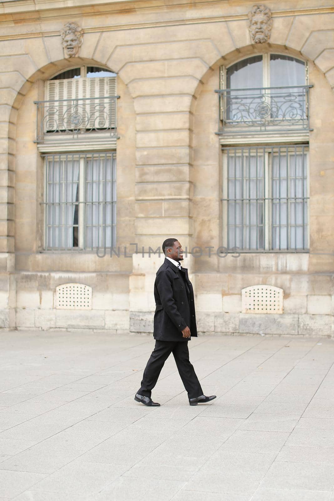 Afro american smiling man walking in city and wearing black suit. Concept of successful businessman and urban life.