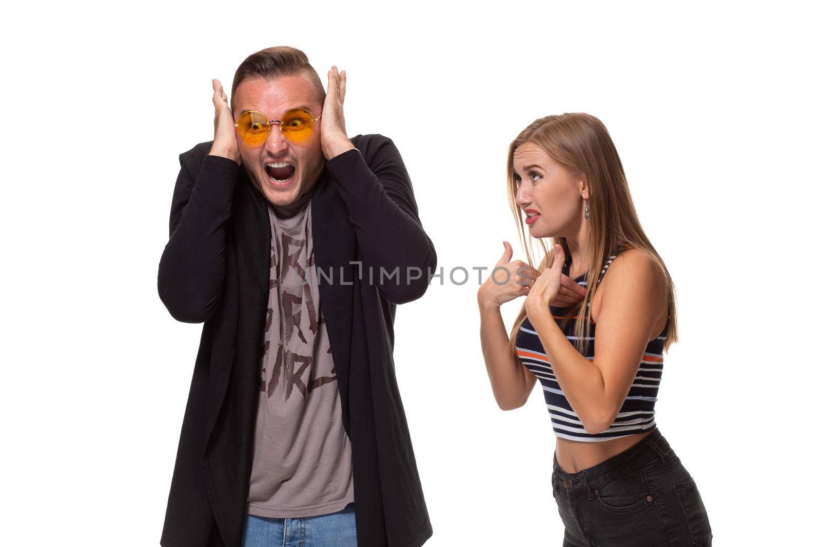 Young family couple have conflict. Angry blonde young European woman gestures with hands, shouts at husband who is guilty, stands together against white background, have dispute and quarrel