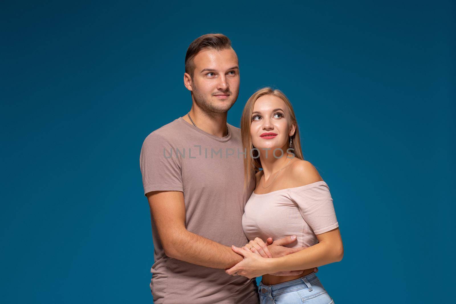 Young couple is hugging on blue background in studio. They wear T-shirts, jeans and smile. by nazarovsergey