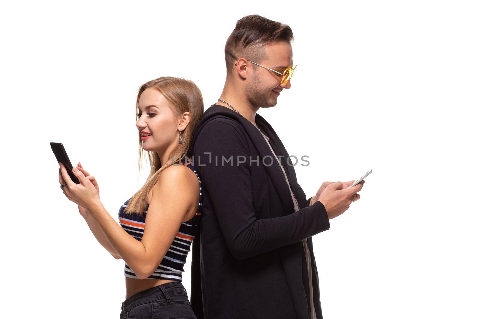 Man and woman stand with their backs to each other with telephones in their hands on white background. Studio shot