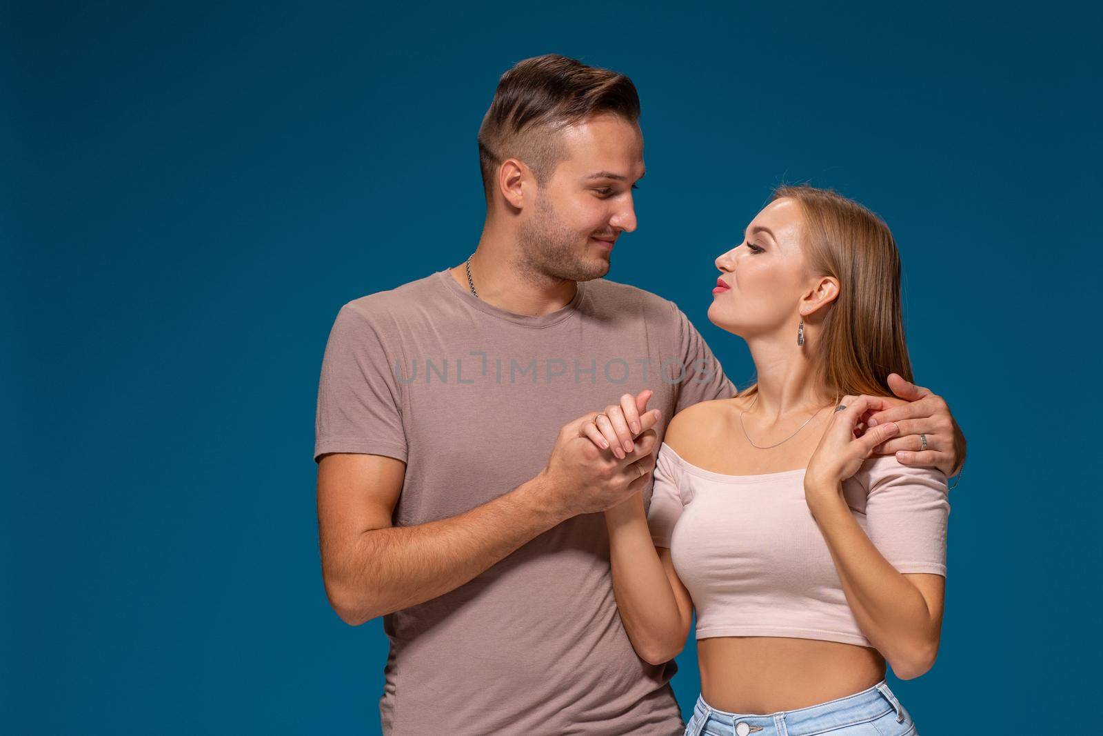 Young couple is hugging on blue background in studio. They wear T-shirts, jeans and smile. Friendship, love and relationships concept