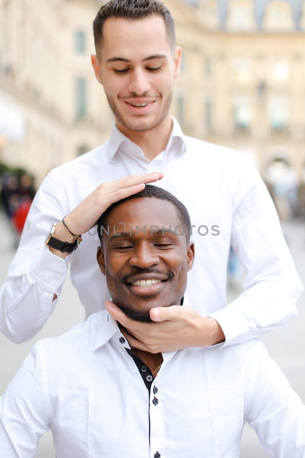 Caucasian boy holding afro american guy head by hands, wearing white shirt. Concept of stylish boy and haircut.