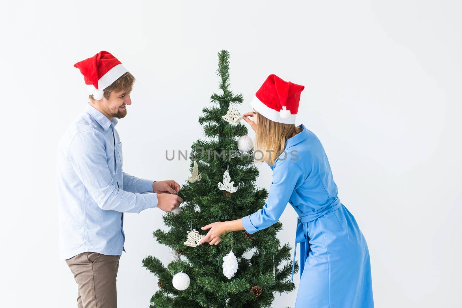 Holidays and festive concept - Young family couple decorating the christmas tree.