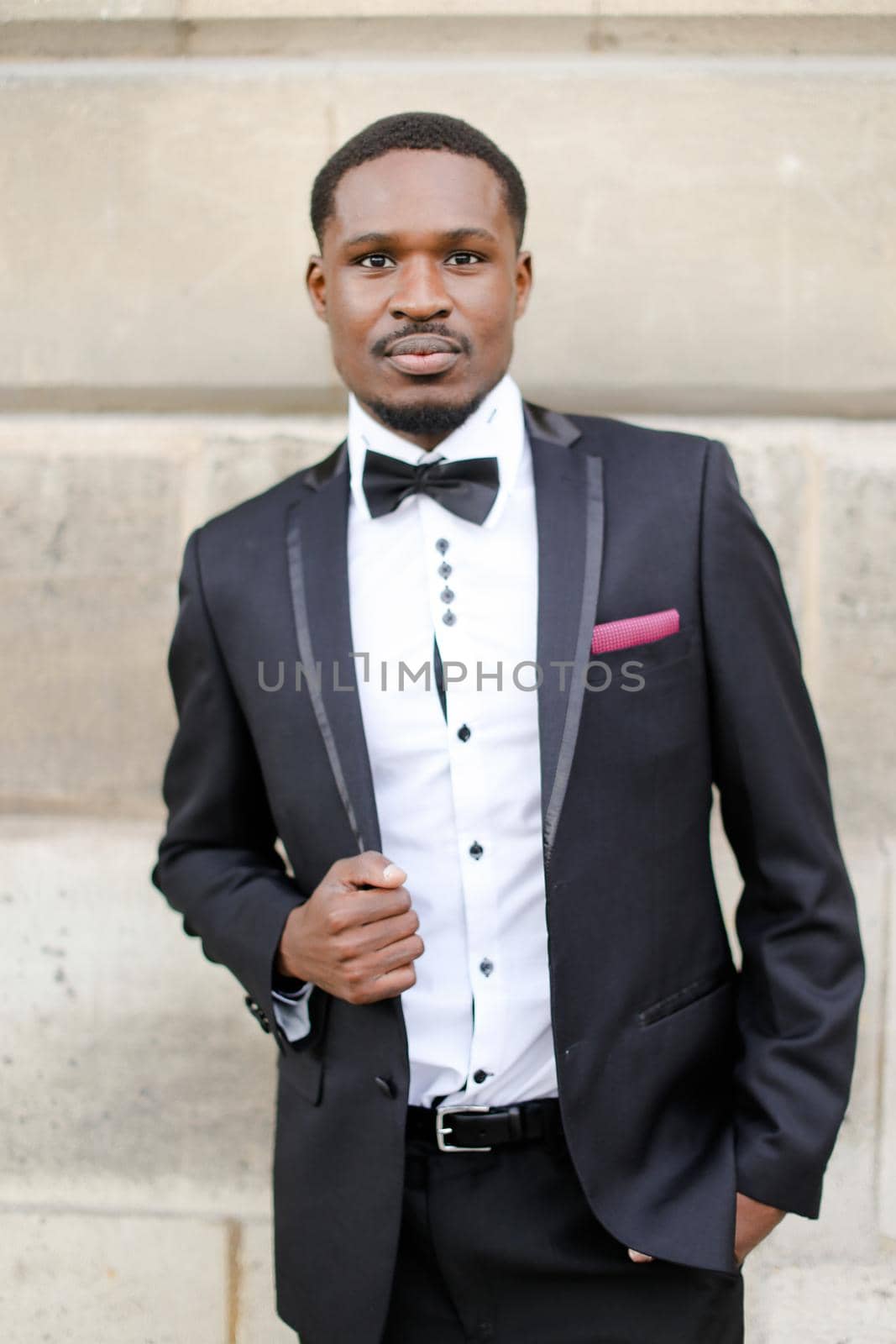 Afro american happy man wearing suit and standing near wall outside. by sisterspro