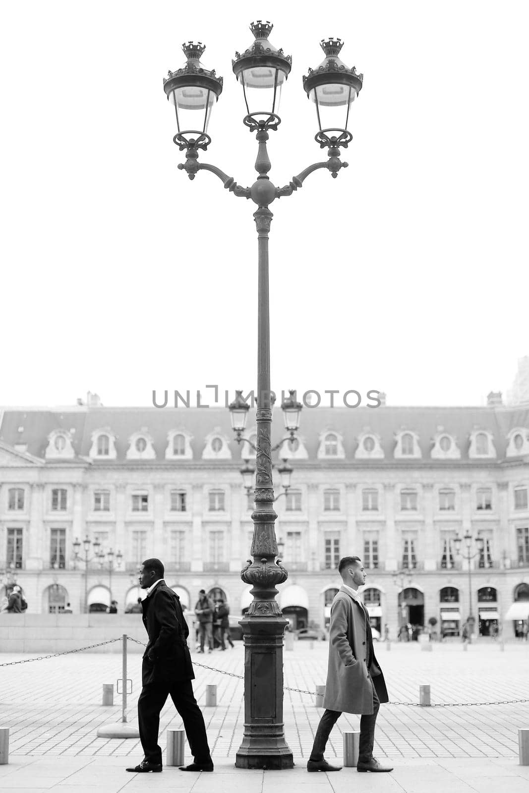 Black and white photo of afro american and caucasian men standing near street lantern in city. by sisterspro