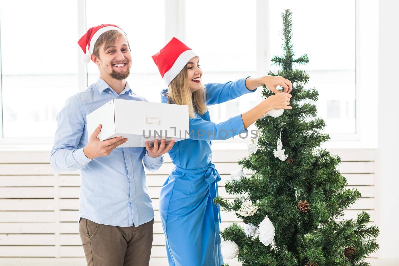 Holidays and festive concept - Young family couple decorating the christmas tree.