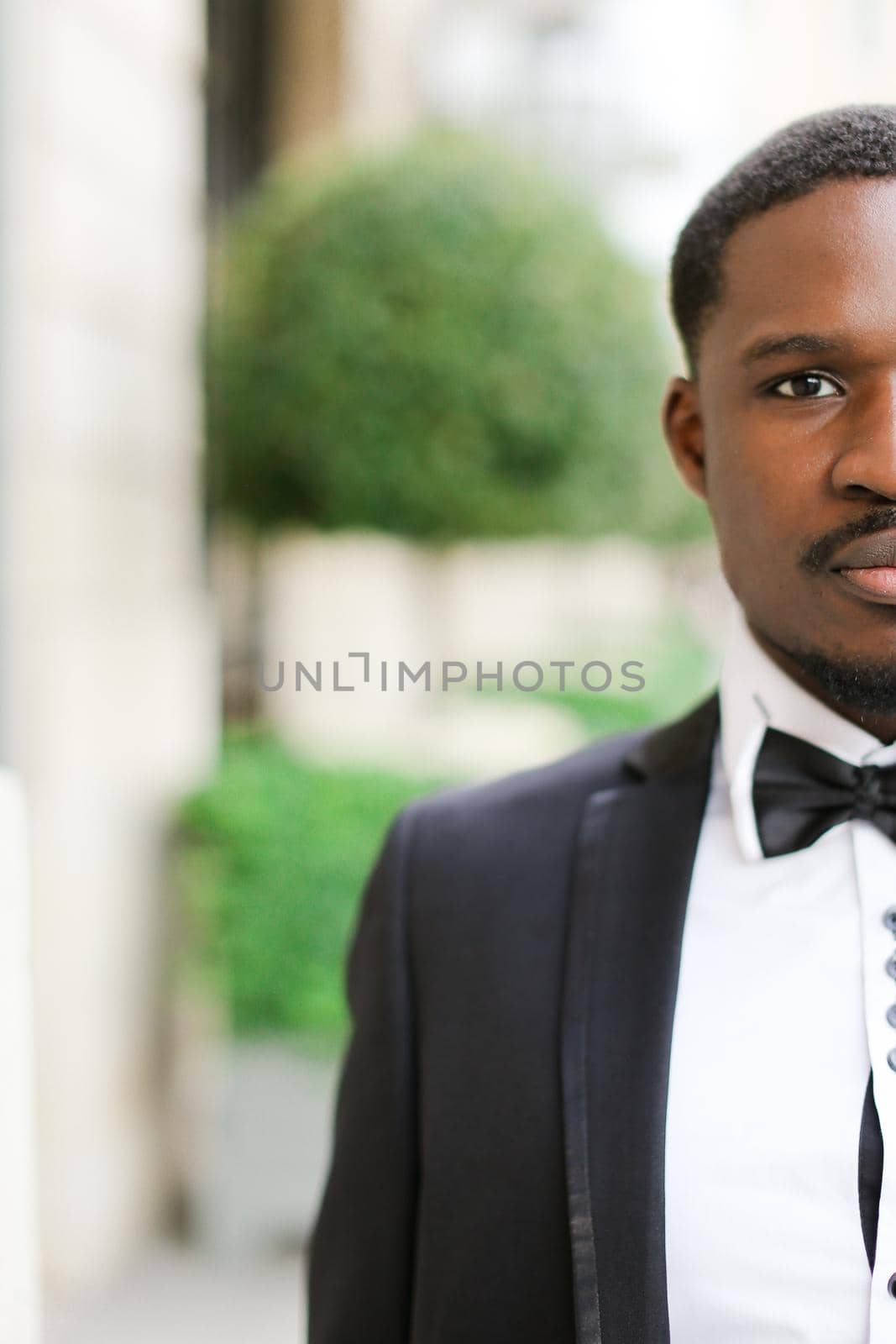 Portrait of afro american happy man wearing dark suit and standing outdoors. Concept of black businessman.