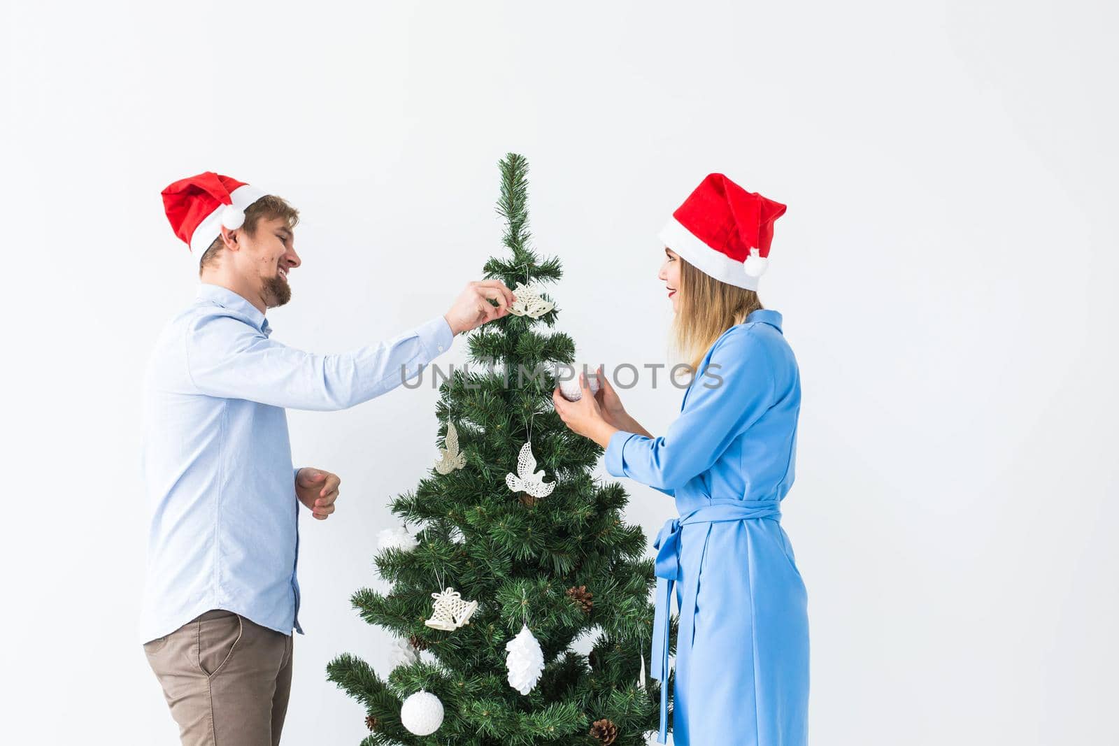 Holidays and festive concept - Young family couple decorating the christmas tree.