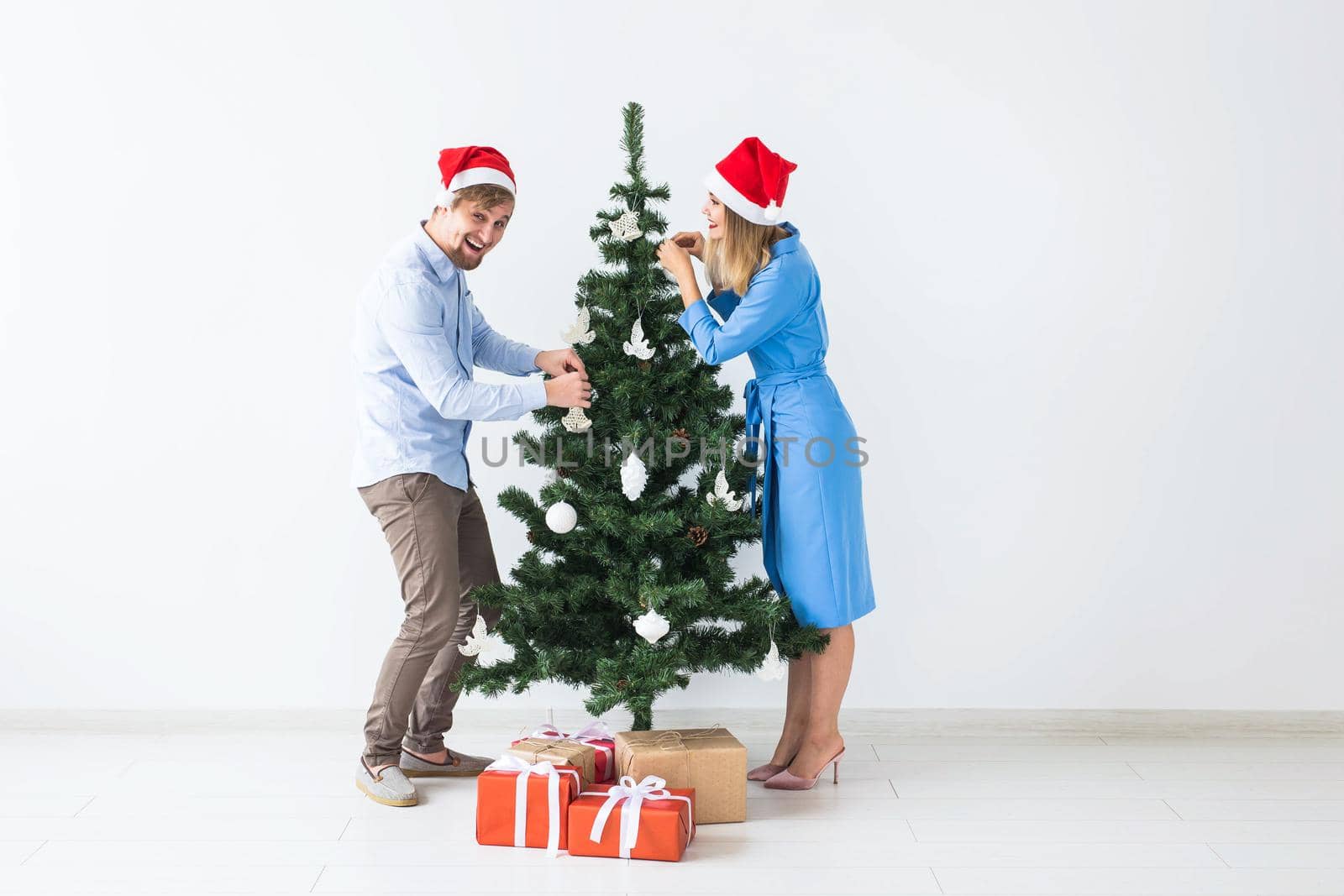 Holidays and festive concept - Young family couple in santa hats decorating the christmas tree by Satura86