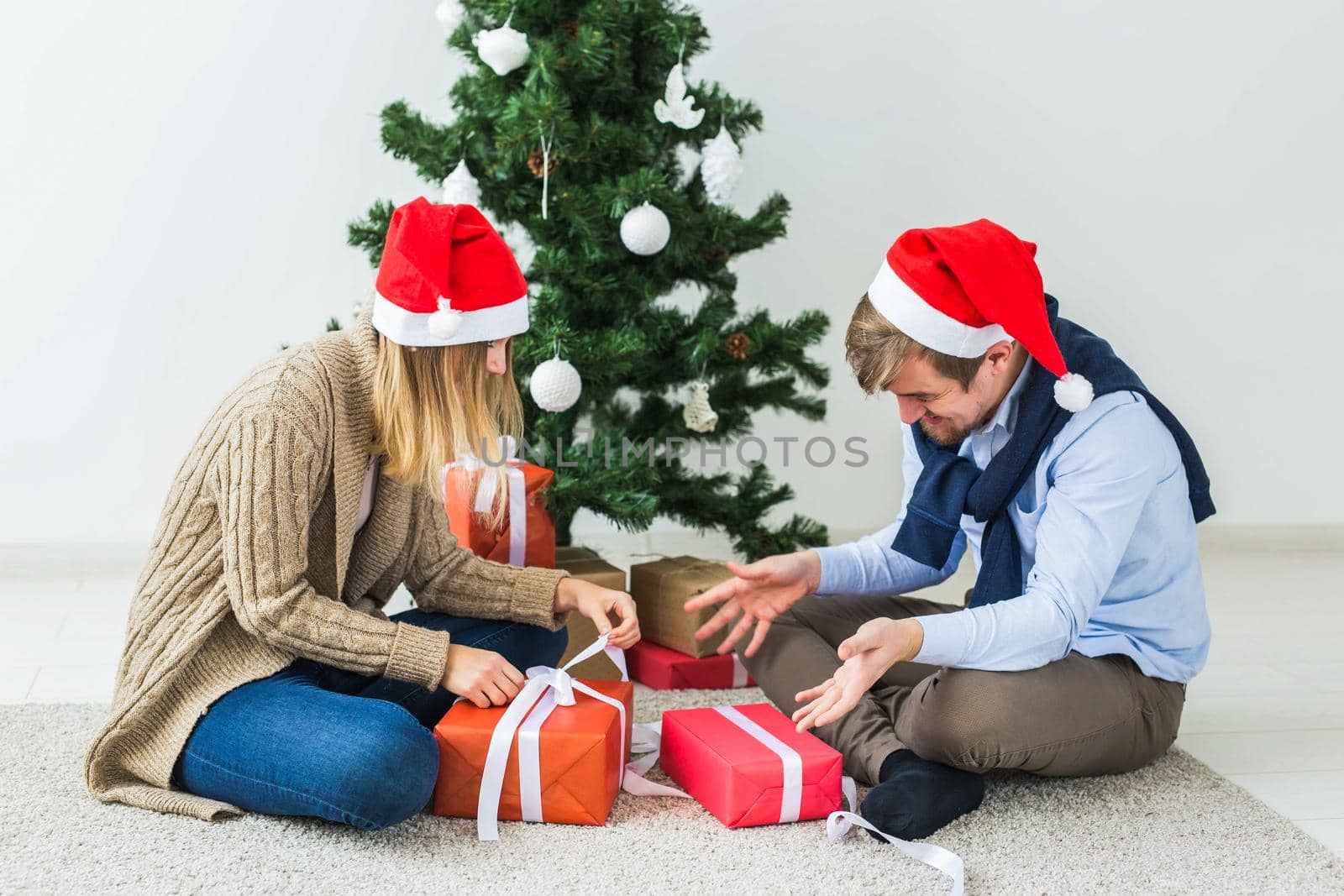 Christmas and holidays concept - Young happy couple wearing santa hats opening gifts at home