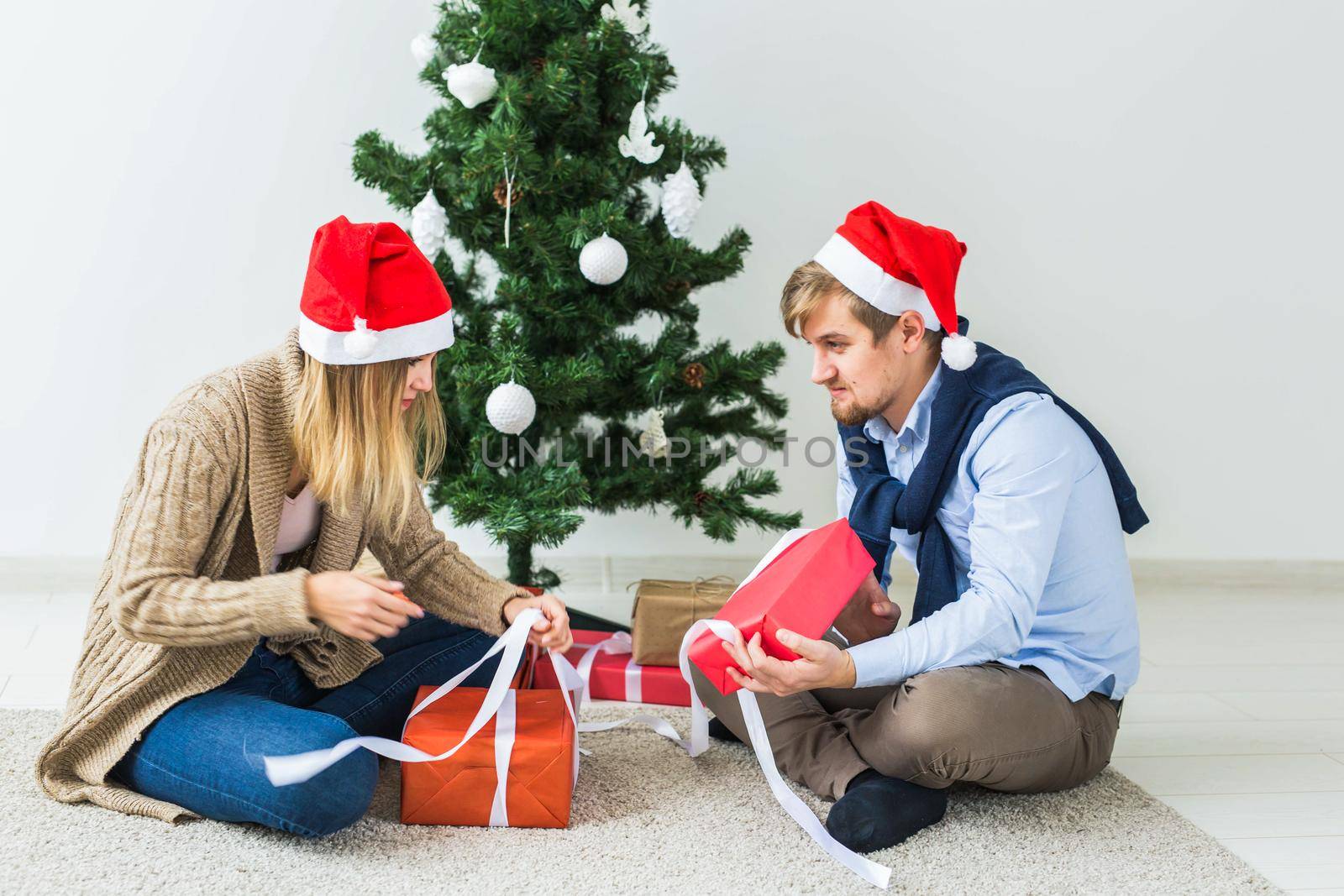 Holidays concept - Sweet couple opening Christmas gifts, sitting in the living room by Satura86