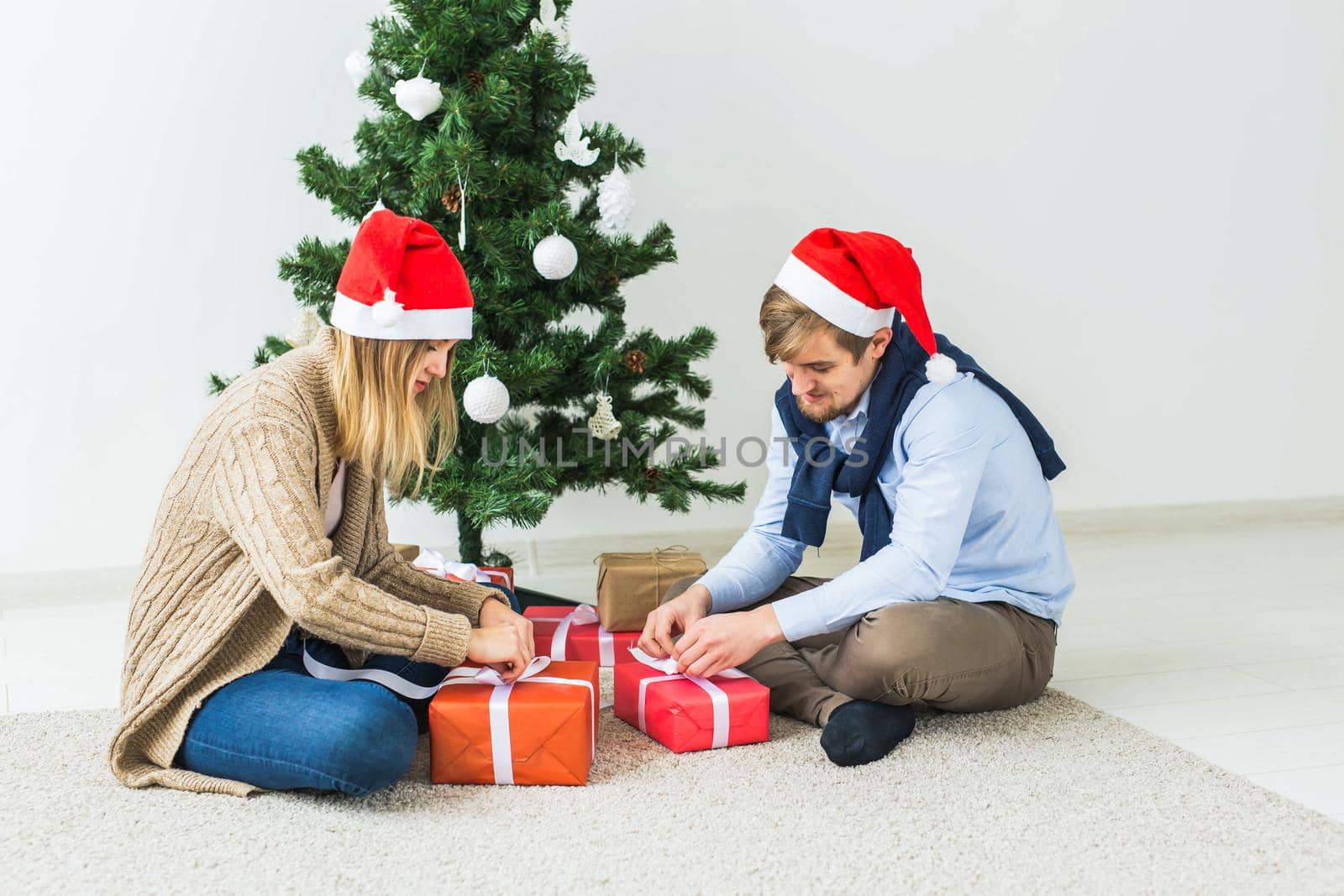 Christmas and holidays concept - Young happy couple wearing santa hats opening gifts at home. by Satura86