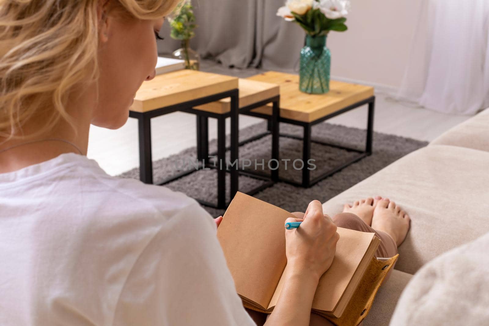 Close up woman hand writing on notebook. Young woman sitting on sofa in modern apartment, casual style indoor shoot