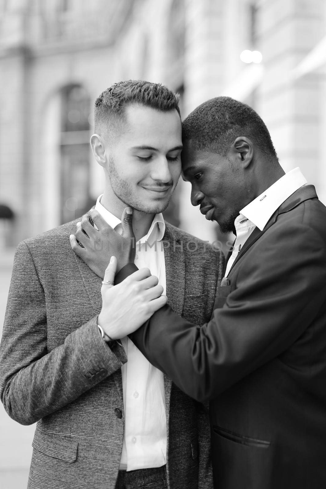 Black and white photo of afro american gay hugging caucasian boy outside, wearing suits. Concept of lgbt and same sex couple.