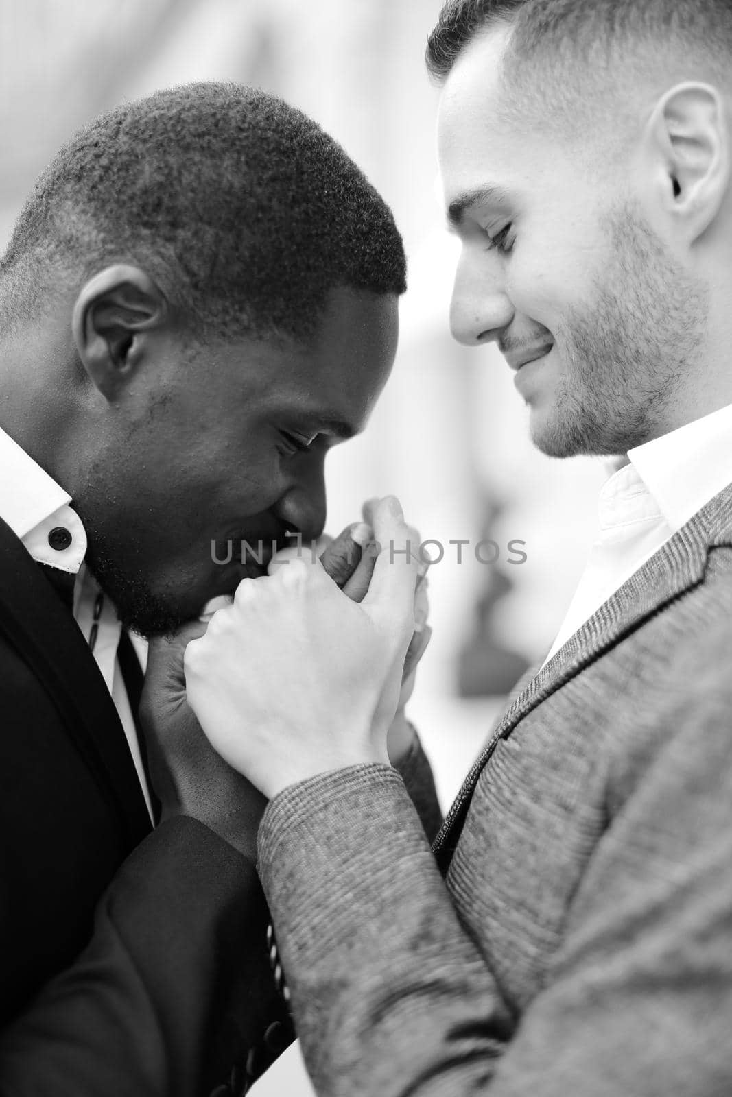 Black and white portrait of afro american guy kissing caucasian boy hands. Concept of same sex couple, gays and lgbt.