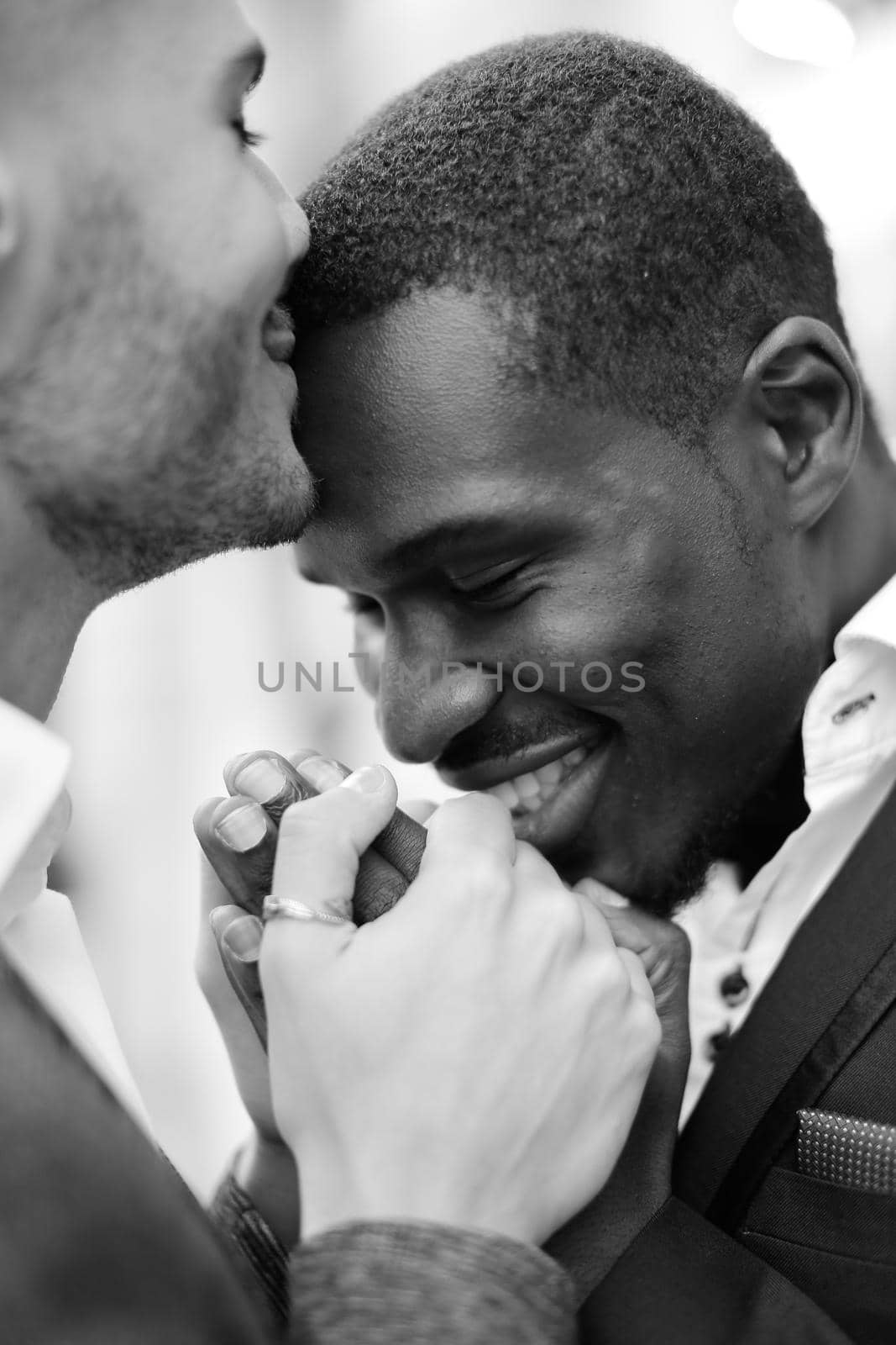 Balck and white photo of caucasian man kissing afro american boy forehead and holding hands. Concept of lgbt and same sex couple.