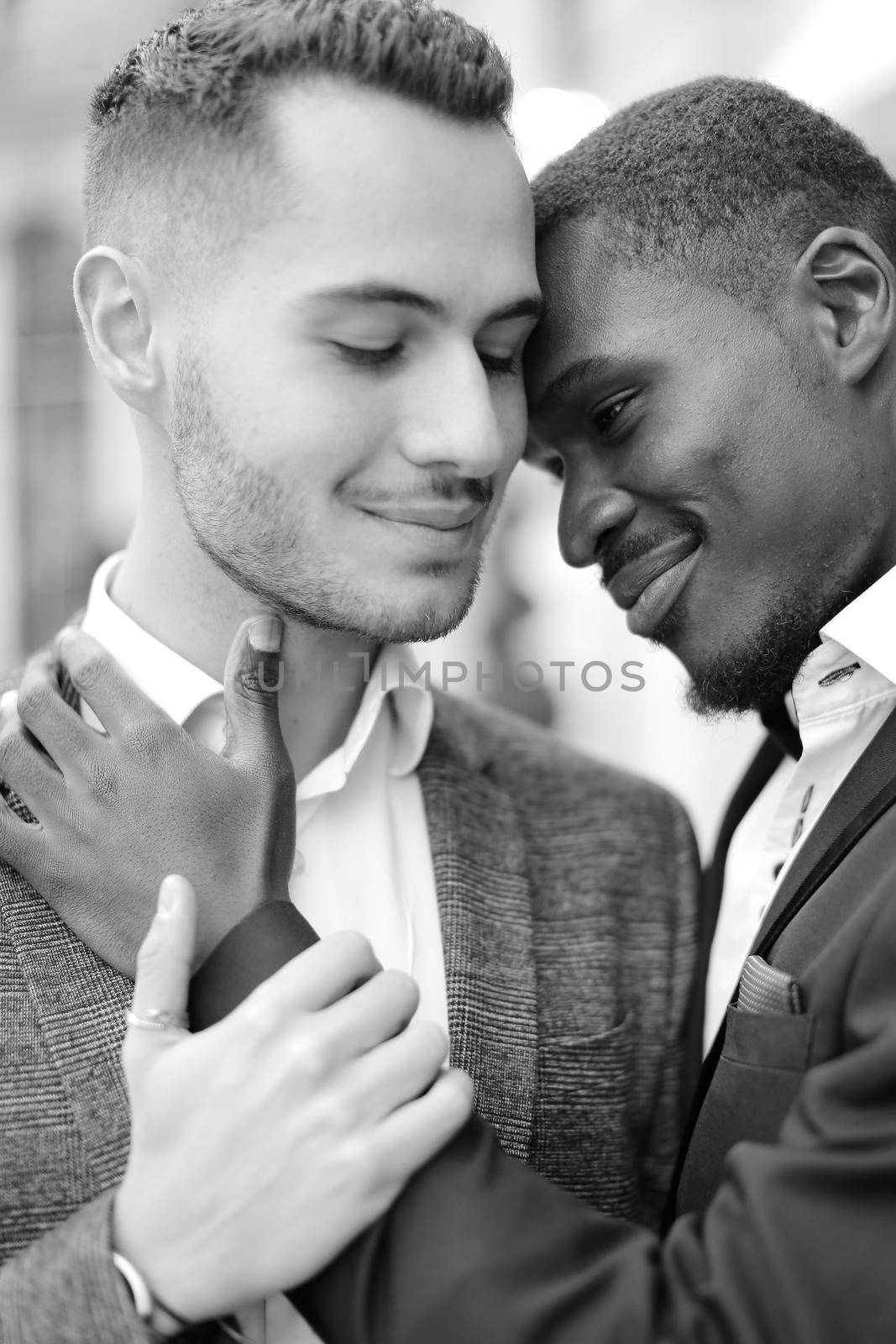 Black and white portrait of afro american gay hugging caucasian boy, wearing suits. Concept of lgbt and same sex couple.