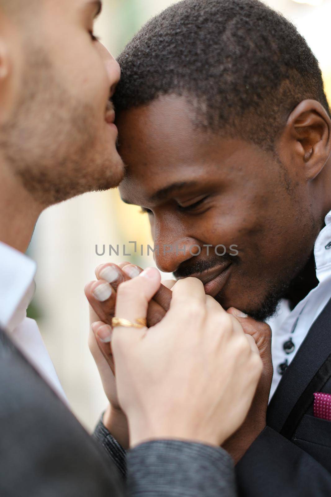 Caucasian man kissing afro american man forehead and holding hands. Concept of lgbt and same sex couple.