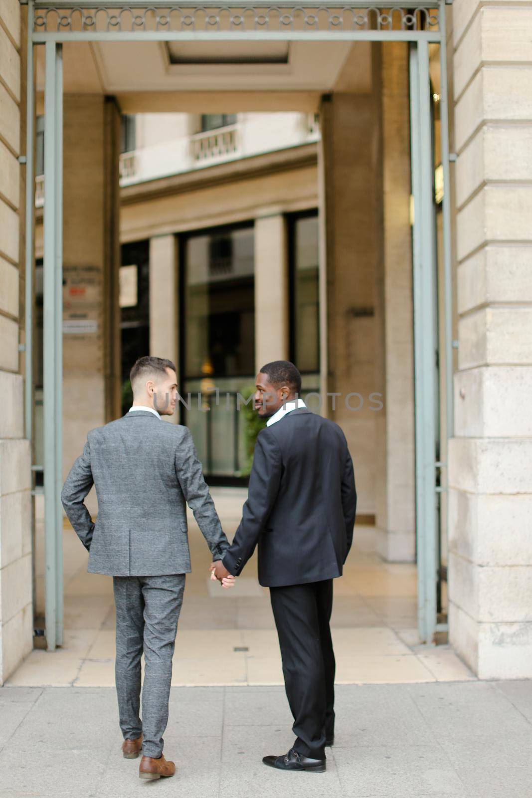 Two men, caucasian and afro american, wearing suits talking near building outside and hugging.