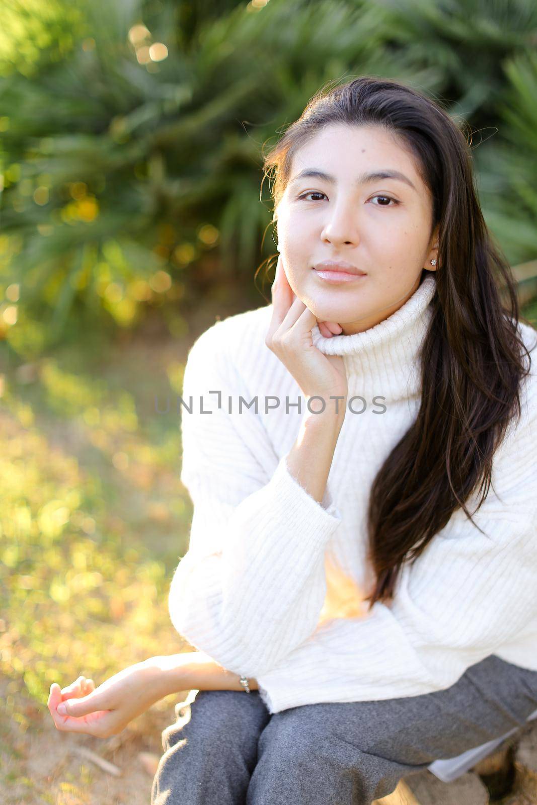Chinese woman in white sweater sitting on grass in park. Concept of asian female person.