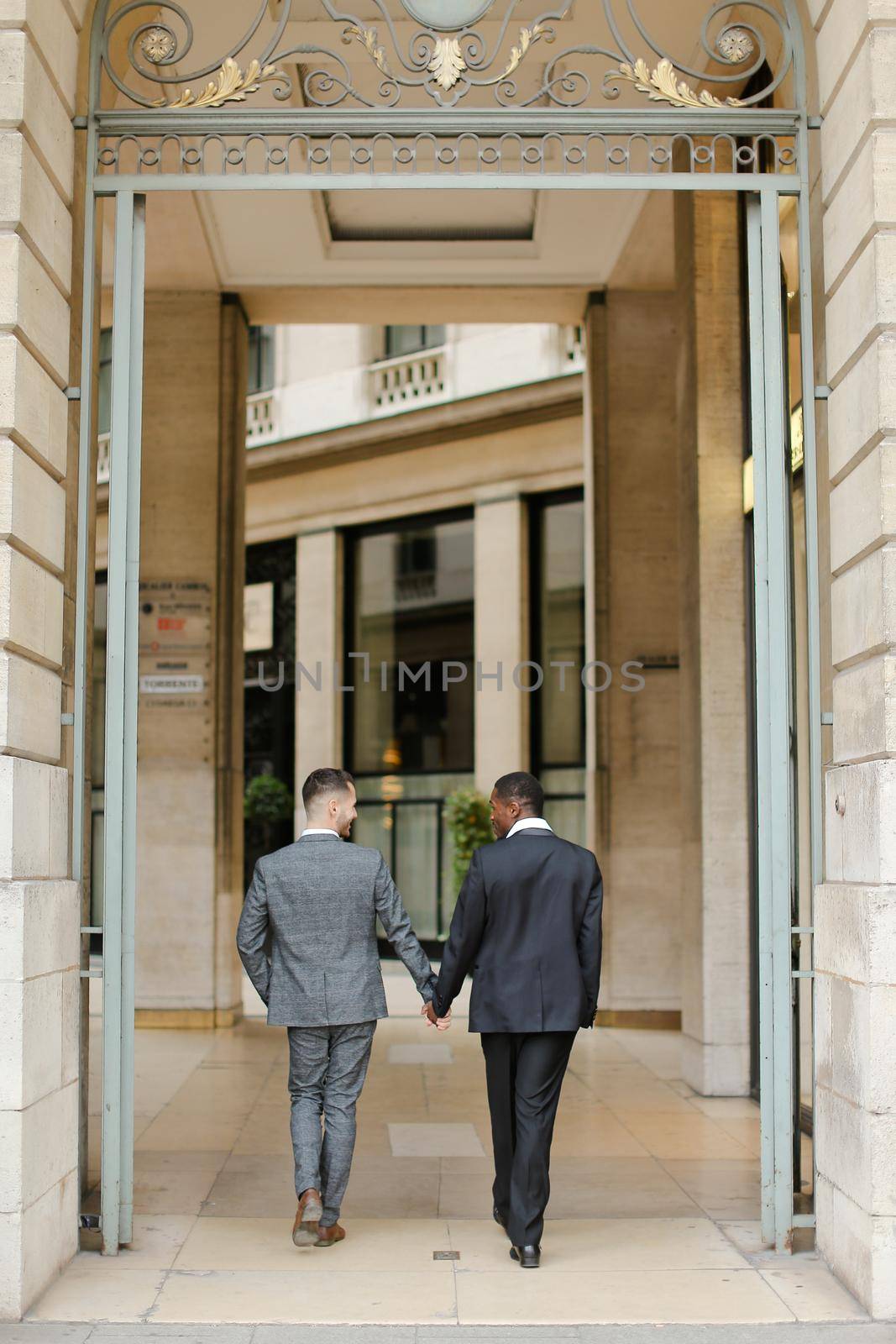 Two men, caucasian and afro american, wearing suits talking near building outside and hugging.