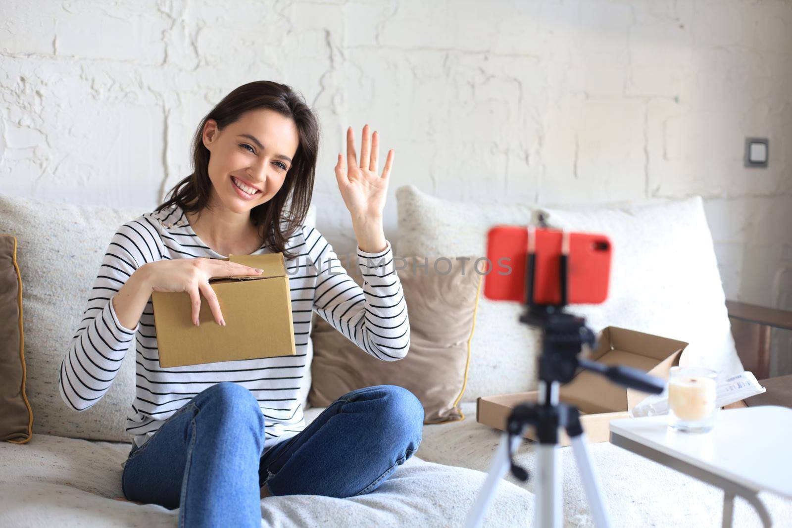 Young beautiful female blogger recording video while unpacking parcel at home. by tsyhun