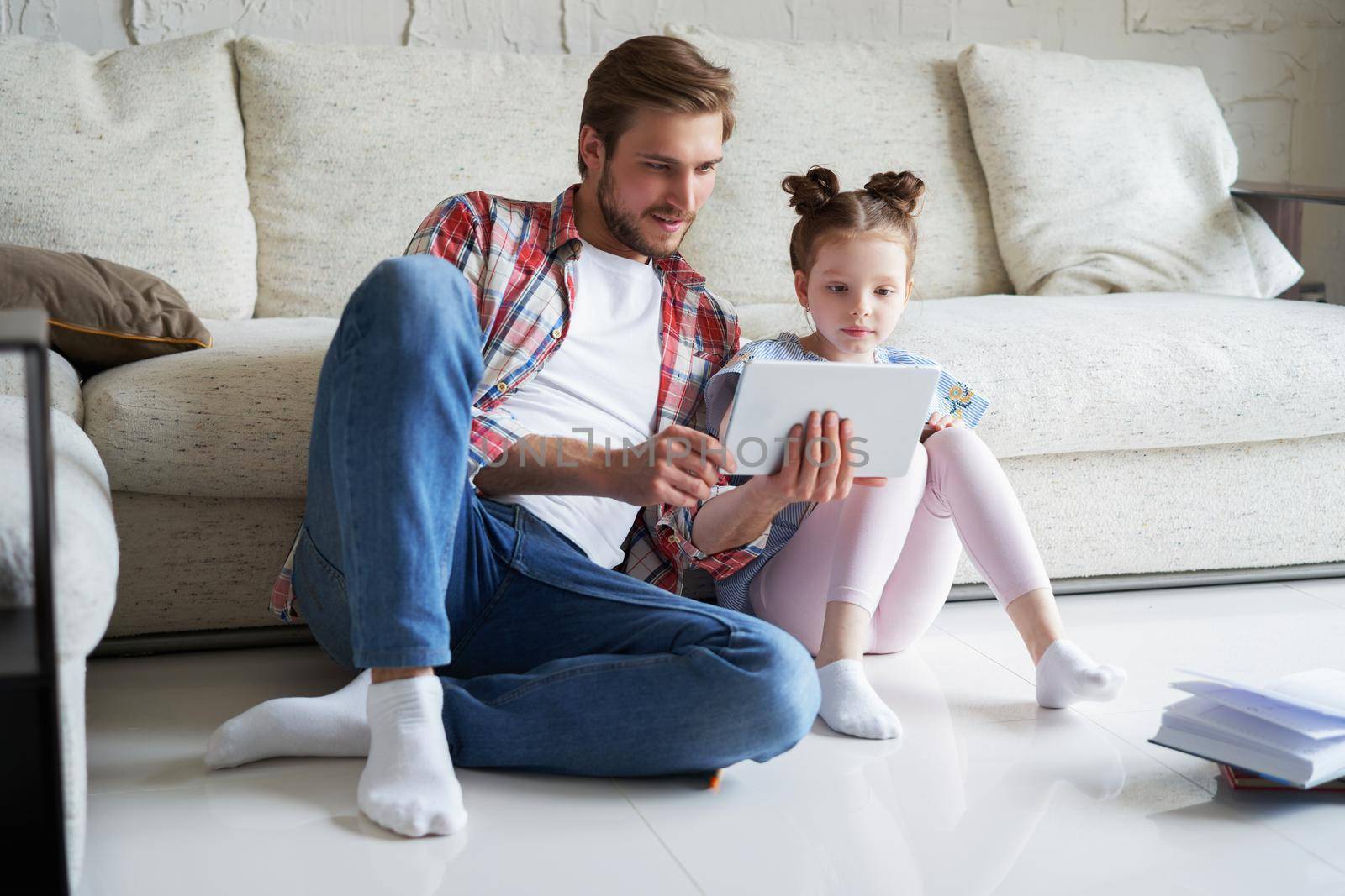 Smiling father and daughter sitting on floor in living room with digital tablet, teaching lessons