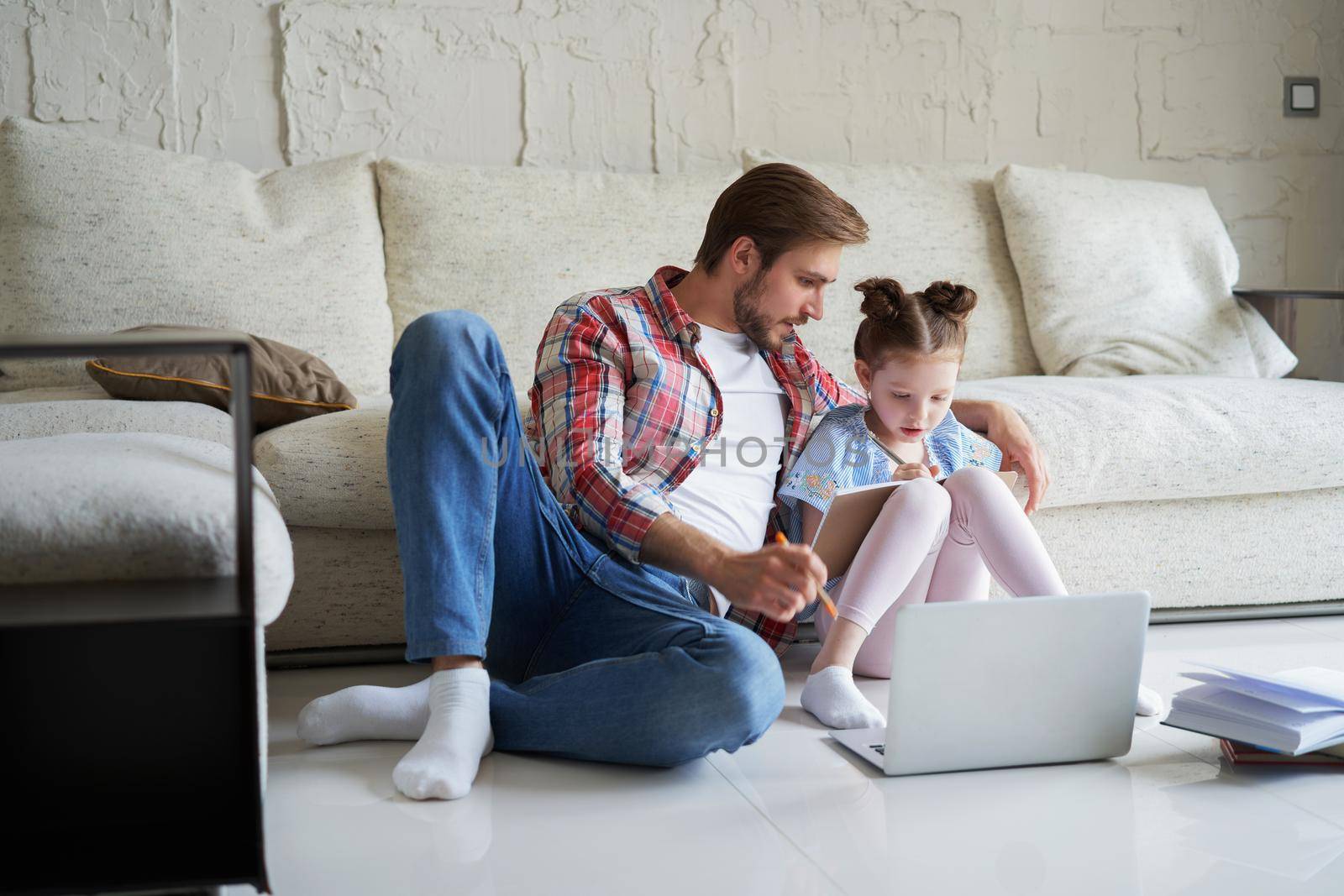 Smiling father and daughter sitting on floor in living room with laptop, teaching lessons