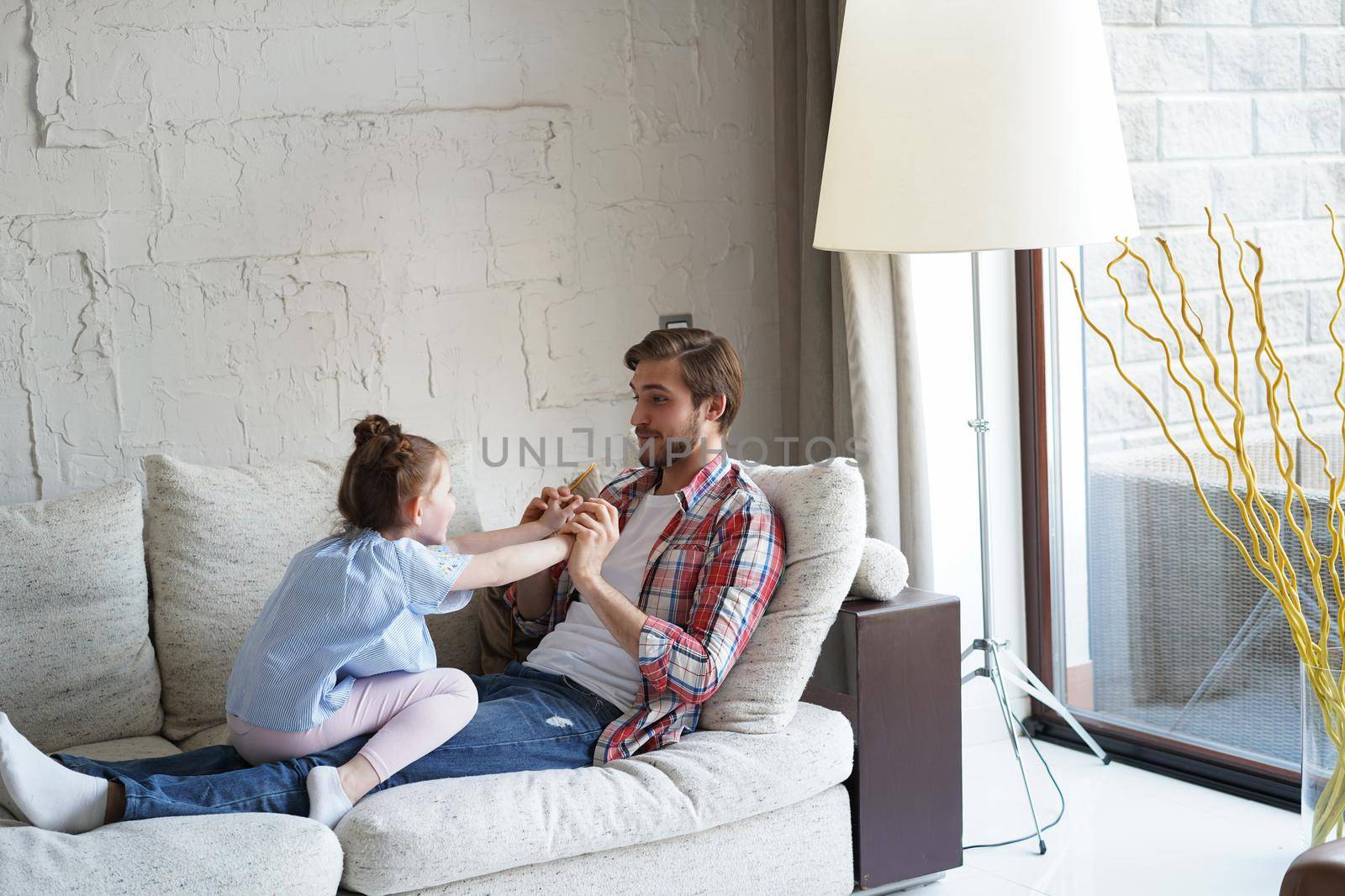 Cute little kid daughter laughing tickling playing with dad on sofa, happy father relaxing having fun with funny small child girl bonding enjoying leisure together in living room