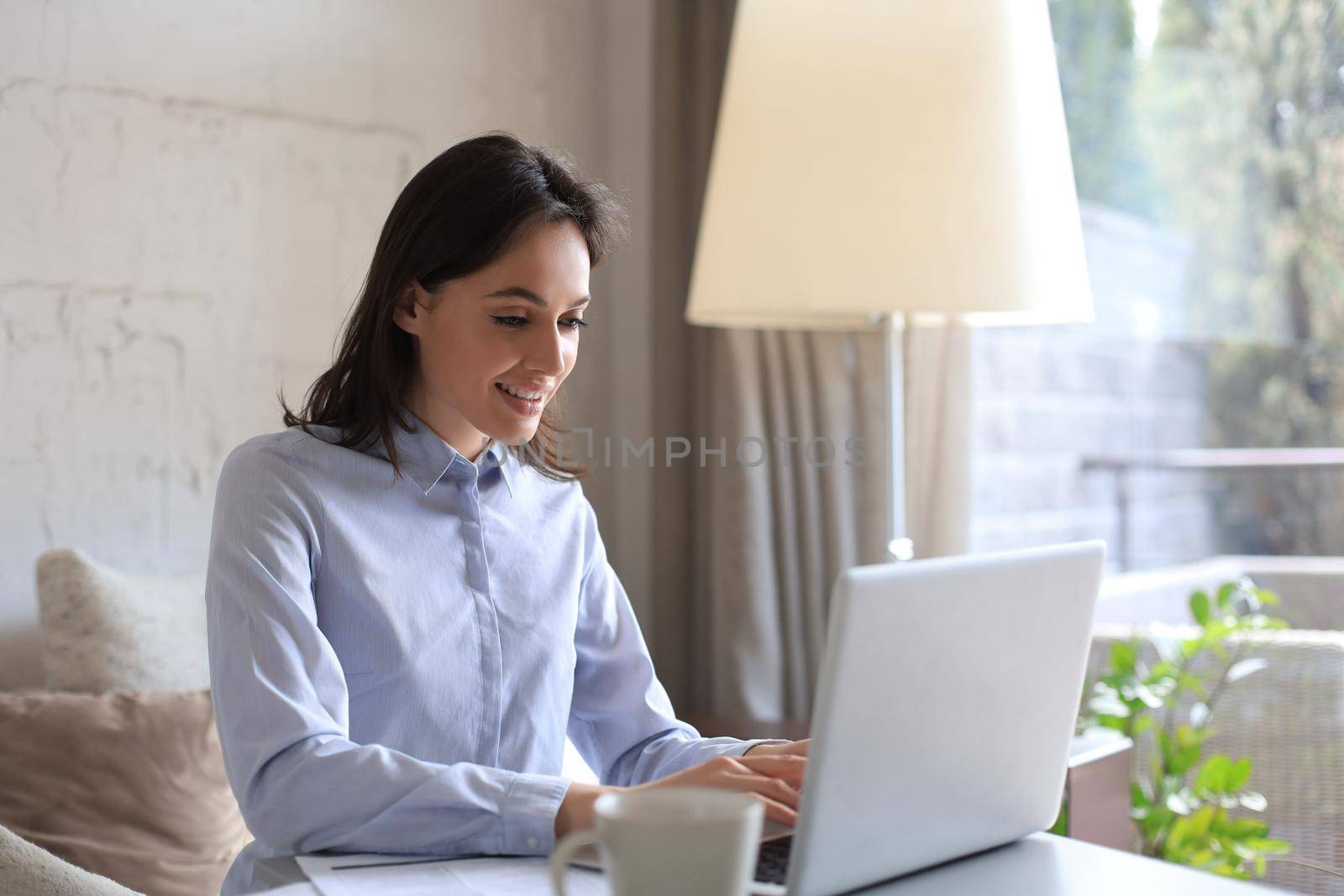 Smiling pretty woman sitting at table, looking at laptop screen. Happy entrepreneur reading message email with good news, chatting with clients online