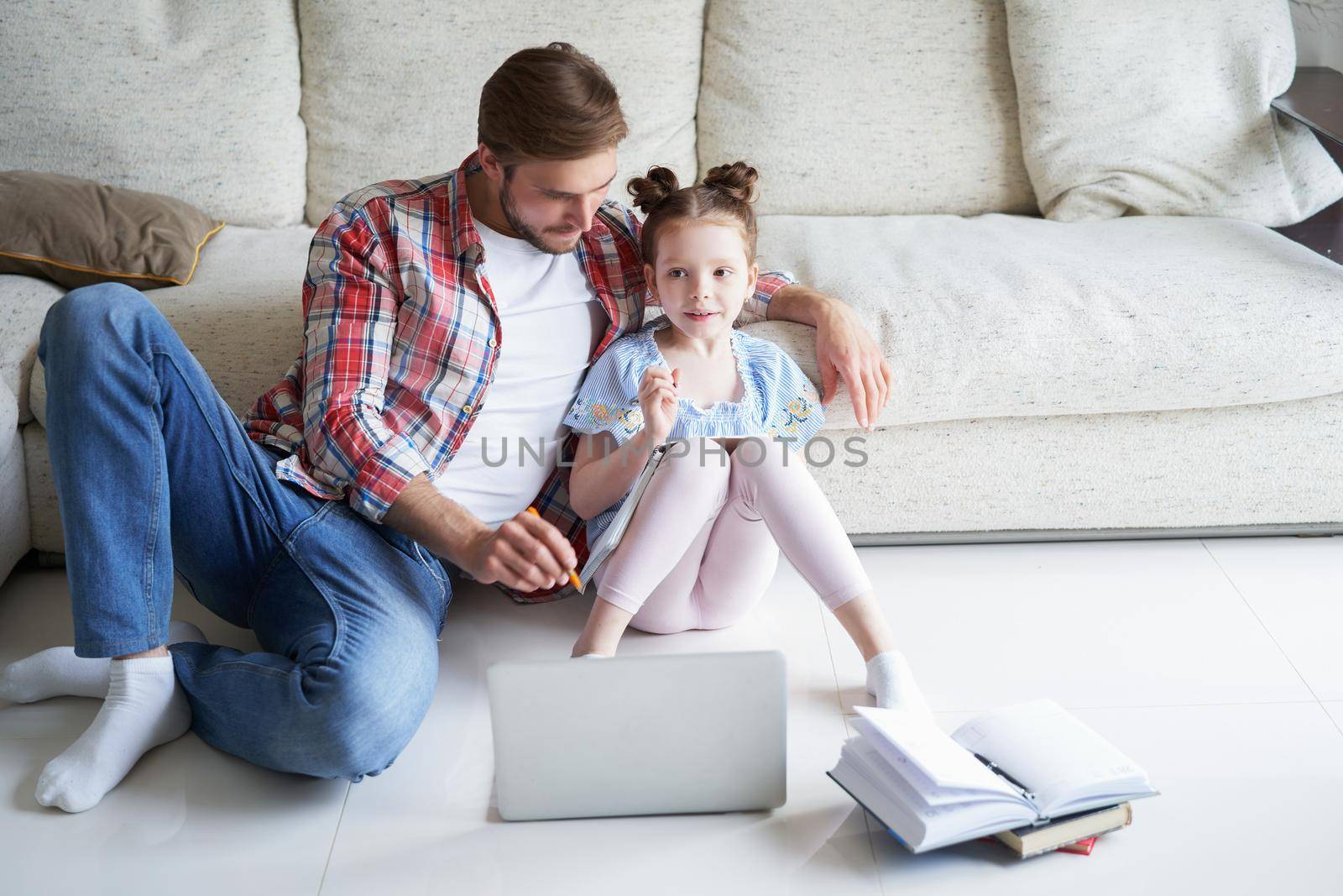 Smiling father and daughter sitting on floor in living room with laptop, teaching lessons. by tsyhun