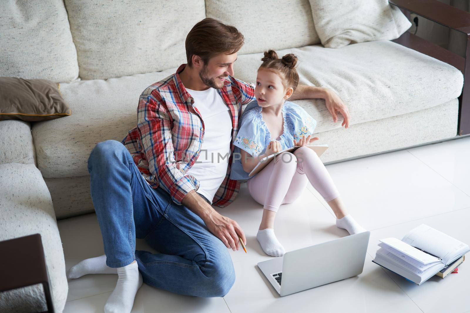 Smiling father and daughter sitting on floor in living room with laptop, teaching lessons. by tsyhun