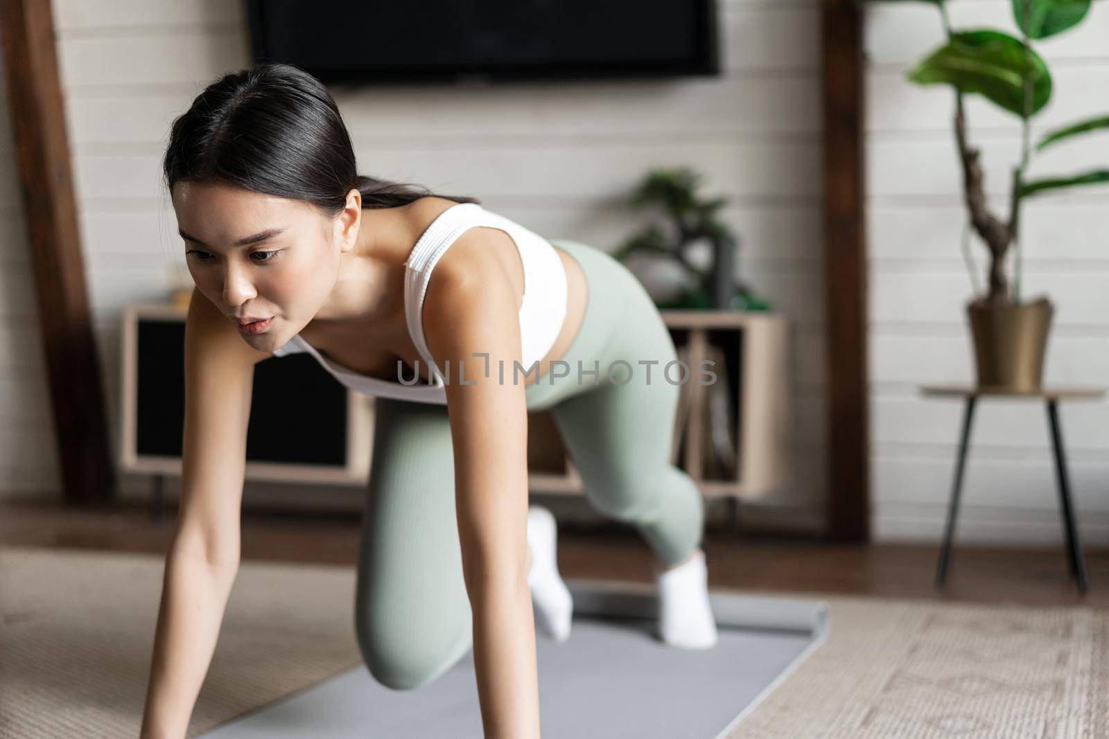 Asian girl doing yoga stretching at home, workout in her living room, wearing activewear.