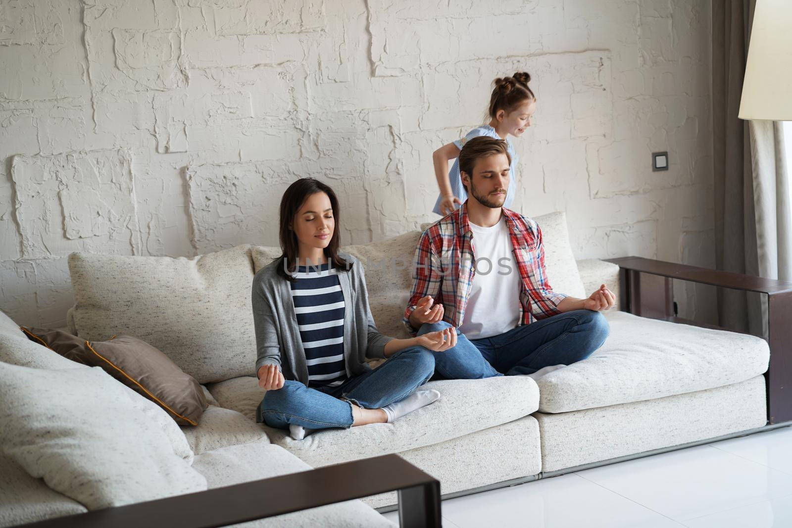 Exhausted mother and father sitting on couch feels annoyed tired while noisy little daughter shouting run around sofa. by tsyhun