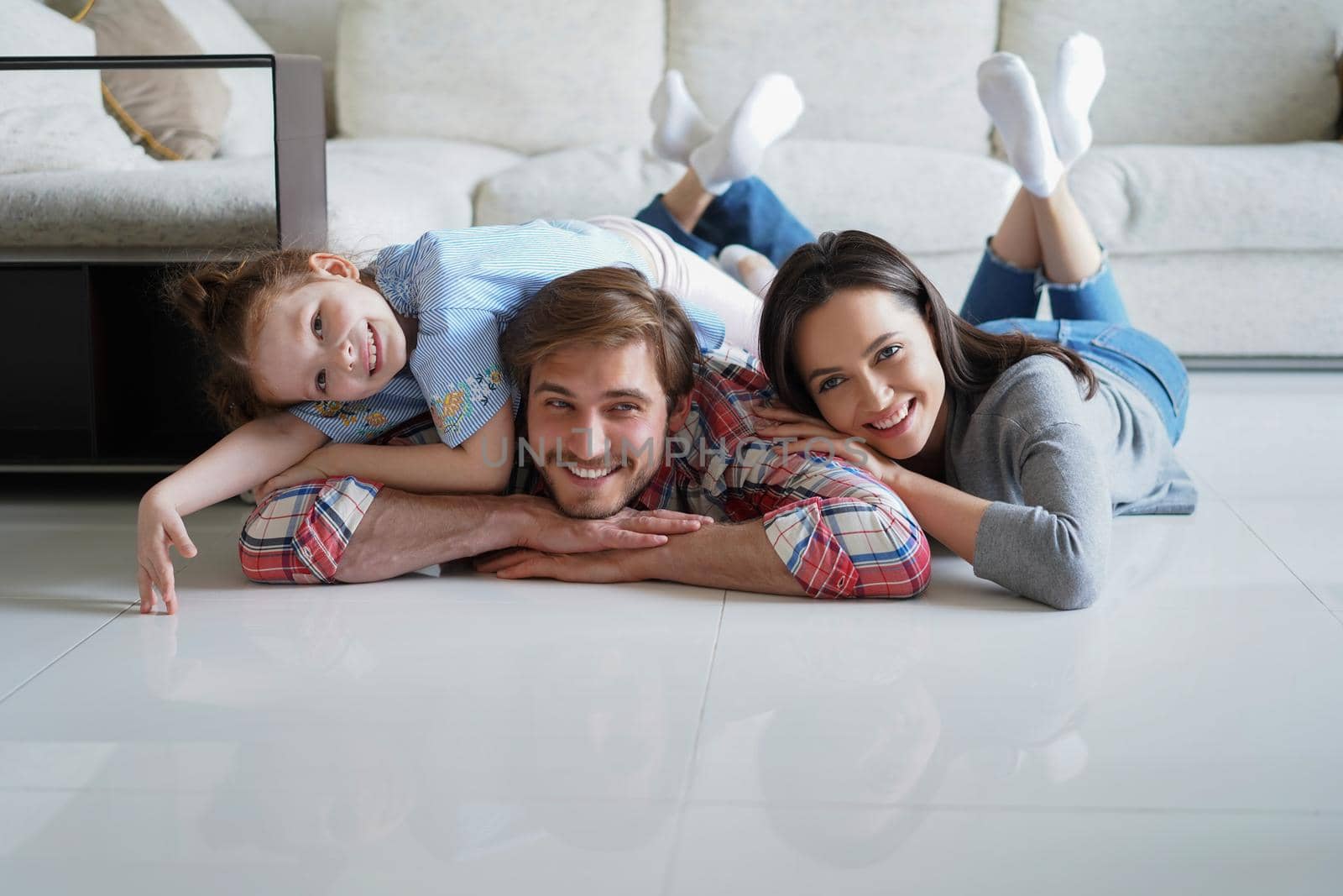 Young caucasian family with small daughter pose relax on floor in living room, smiling little girl kid hug embrace parents, show love and gratitude, rest at home together. by tsyhun