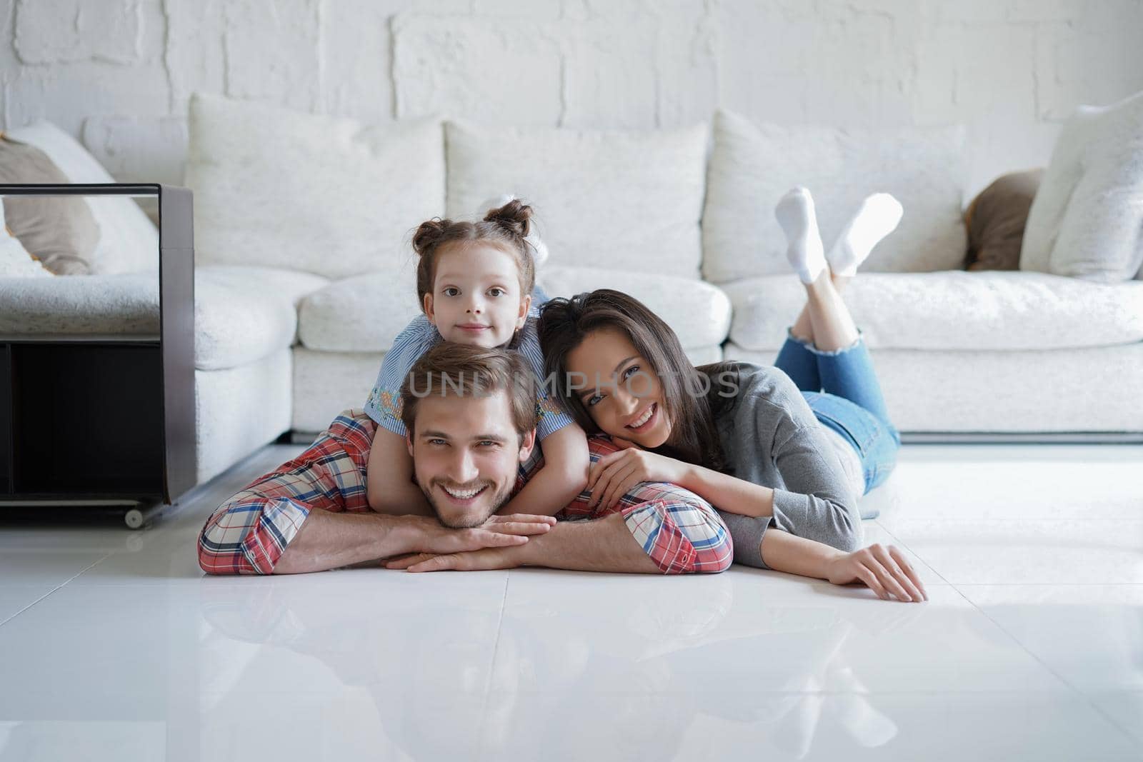 Young caucasian family with small daughter pose relax on floor in living room, smiling little girl kid hug embrace parents, show love and gratitude, rest at home together