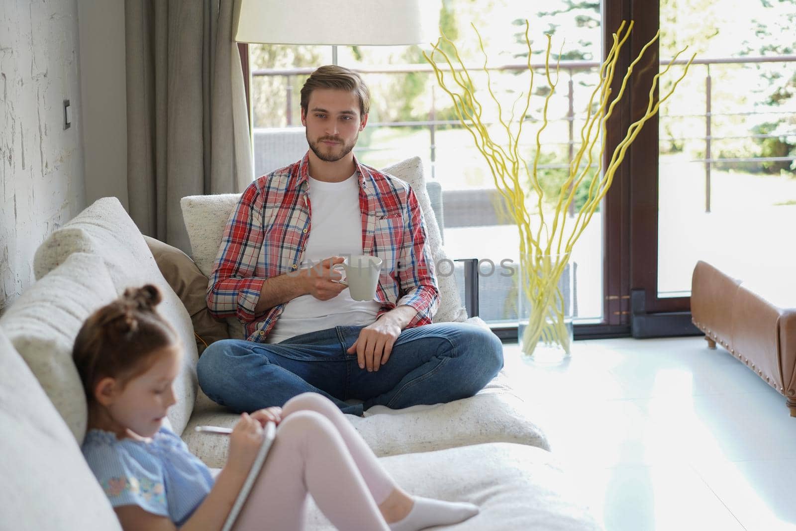 Happy father smilling daughter sitting on sofa enjoying creative activity, drawing pen pictures in albums, father and daughter spend free time together