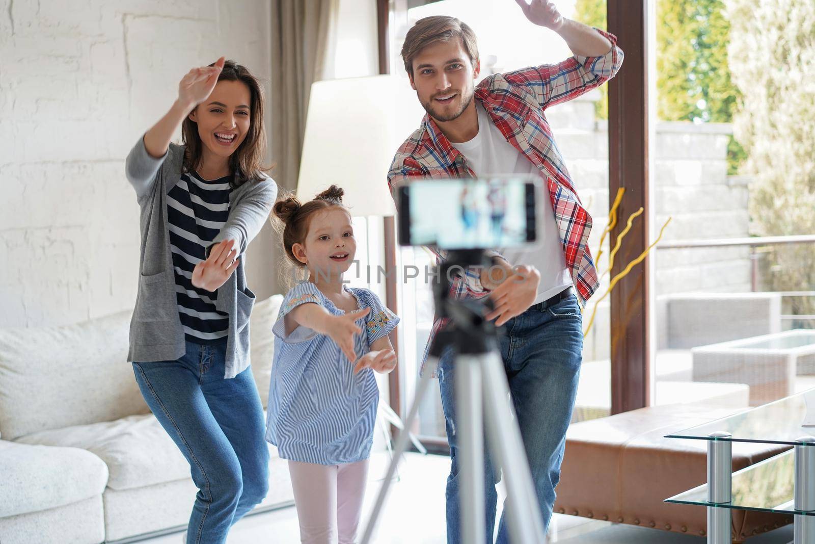Happy young family dancing at home with his little cute daugther, shooting video