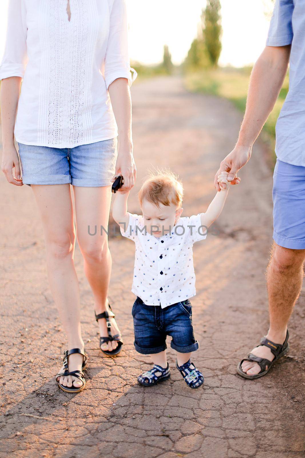 Little child holding parents hands and walking on road. Concept of childhood and resting on open air.