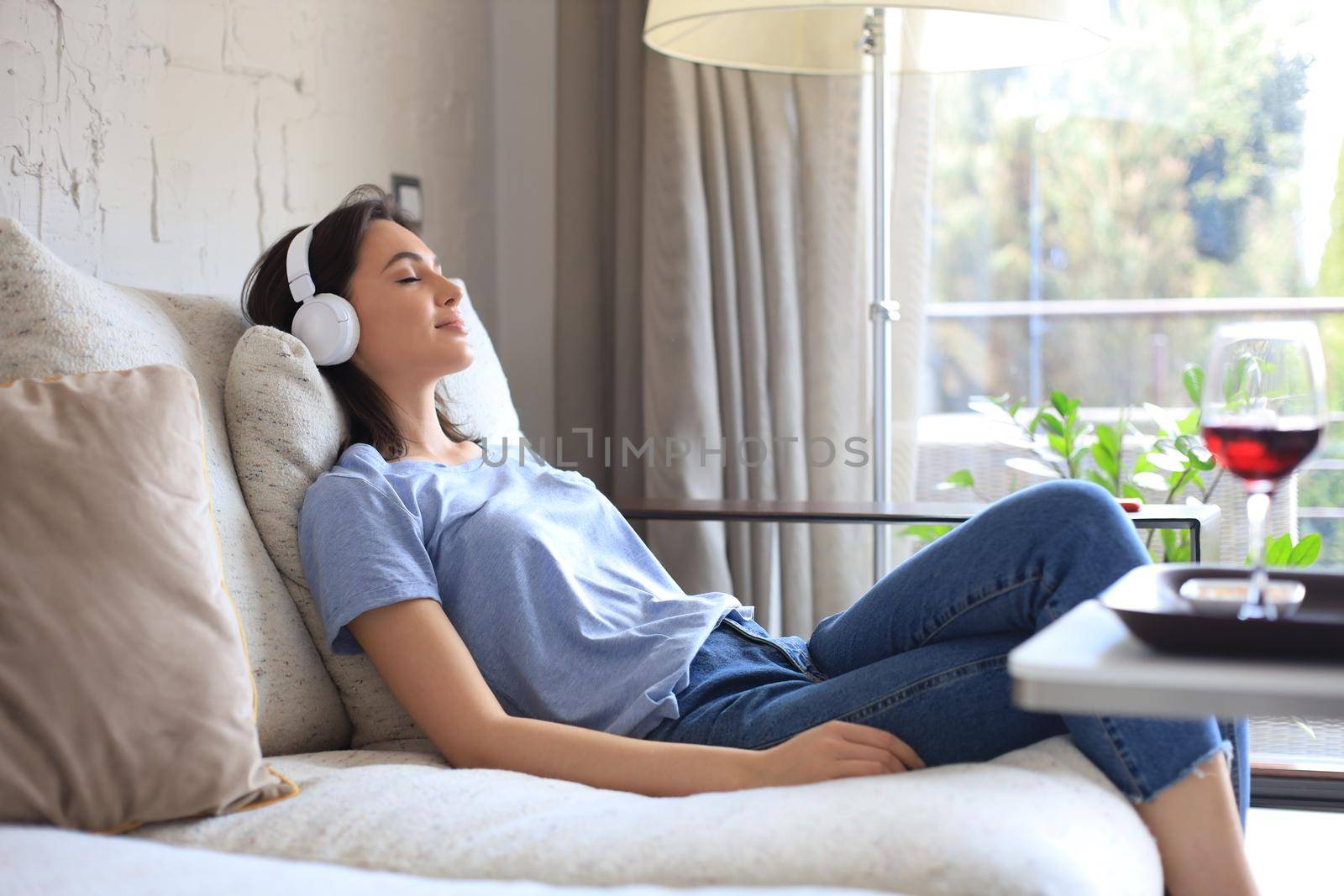 Beautiful brunette woman in earphones sitting on sofa listening to music with closed eyes. by tsyhun