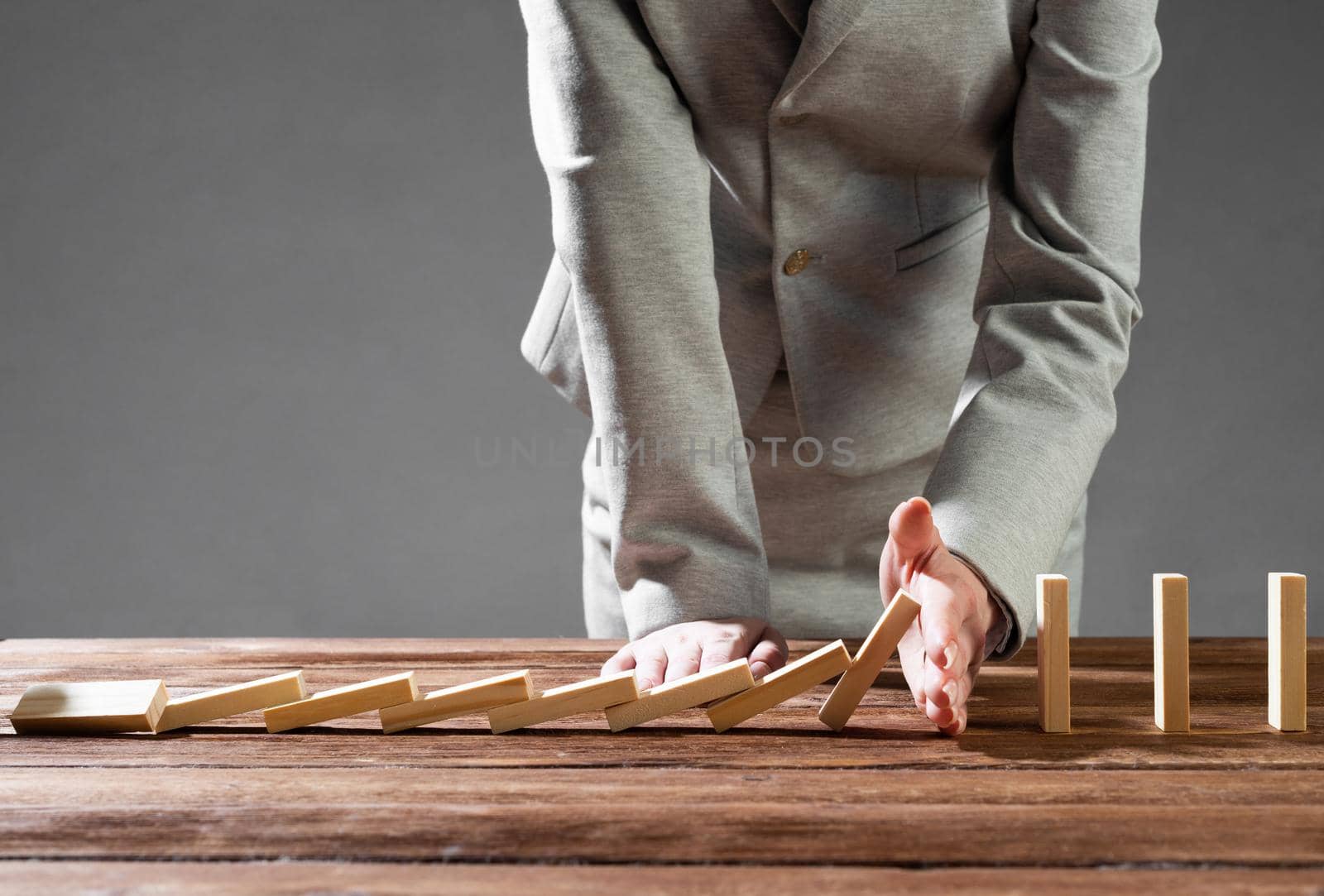Close up female hand interrupting domino effect. Operative business solution, strategy and successful intervention. Business assistance concept with wooden blocks. Protection from economic crisis.