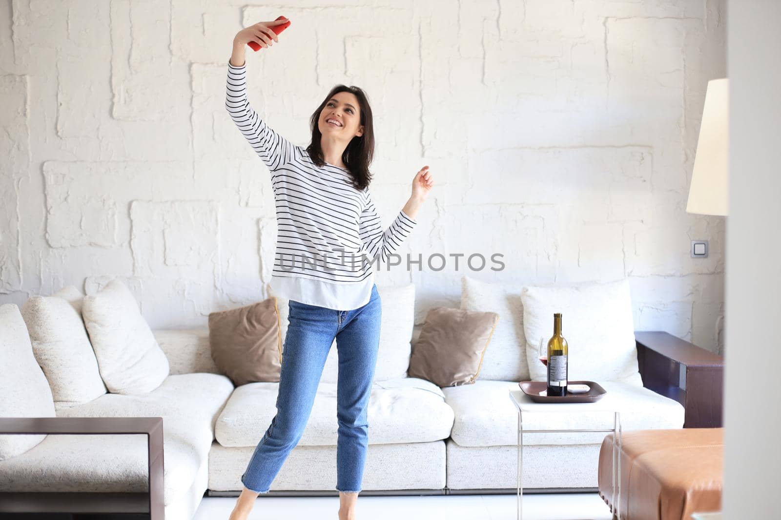 Beautiful young woman taking selfie with smartphone at home near the couch. by tsyhun